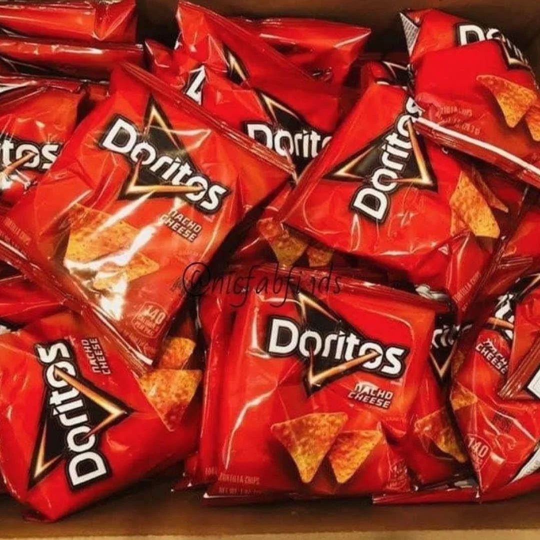 Overhead view of multiple small red bags of Doritos Nacho Cheese tortilla chips piled in a container, showcasing the iconic branding and snack-sized portions.
