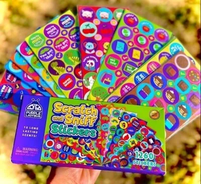 Box of Purple Ladybug Scratch and Sniff Stickers with 1260 colorful stickers and 18 long-lasting scents, displayed with fanned-out sticker sheets featuring playful designs and encouraging messages.
