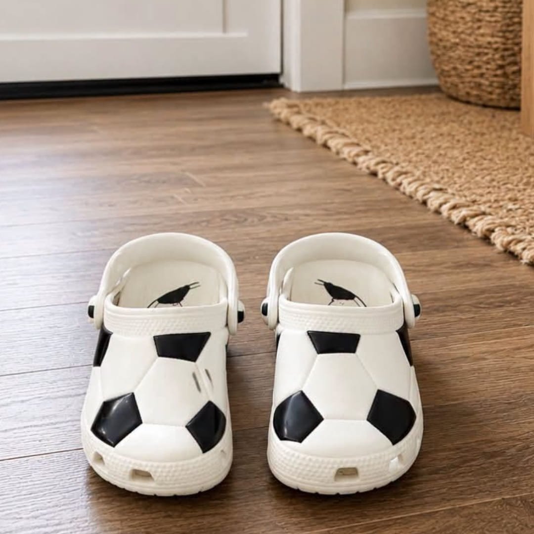 Pair of Crocs Classic Clogs with a black and white soccer ball design on a wooden floor in a home entryway