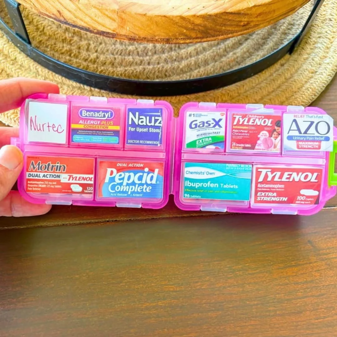 Pink travel pill case organizer with labeled medication compartments opened on wooden table