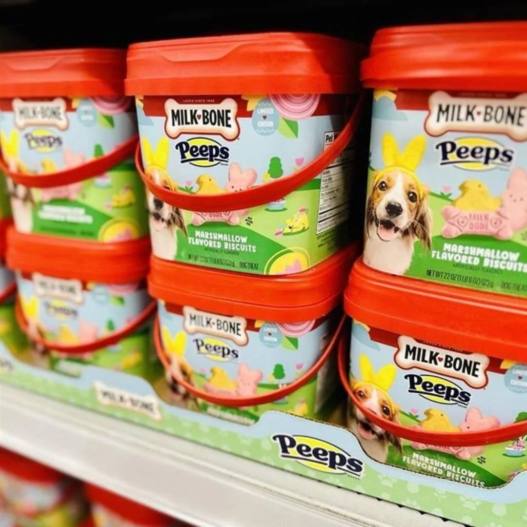 Buckets of Milk-Bone Peeps Marshmallow Flavored Biscuits for dogs, featuring Easter-themed packaging with a beagle in bunny ears and colorful chick- and bunny-shaped treats, displayed on a retail shelf.