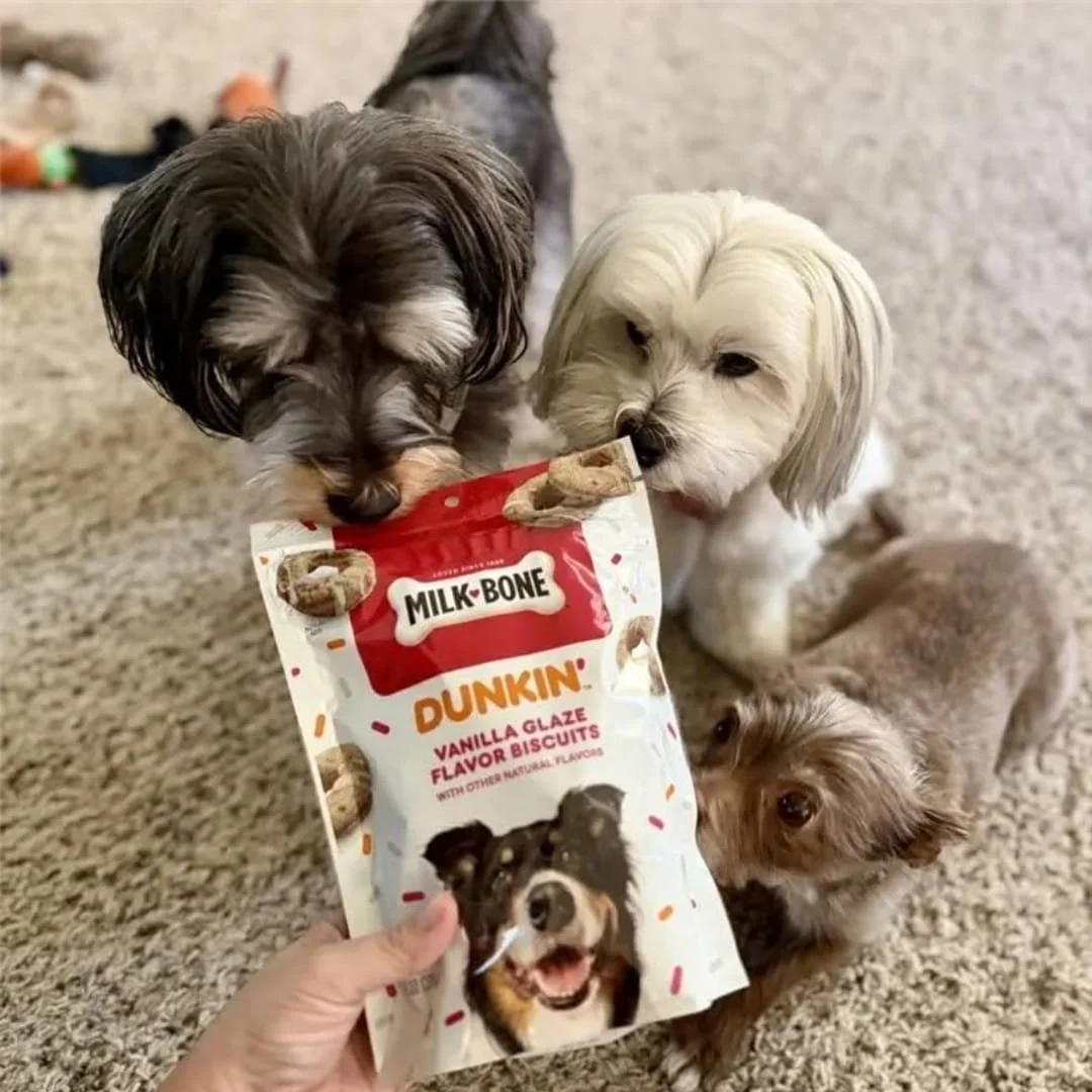 Milk-Bone Dunkin’ Vanilla Glaze dog biscuits bag with three small dogs gathered around it