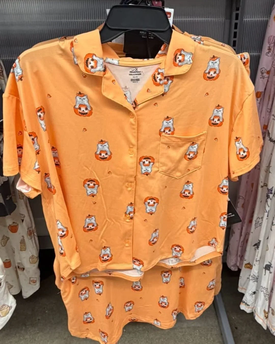 Women’s Halloween pajama set in light orange with cat in pumpkin print hanging on a retail clothing rack