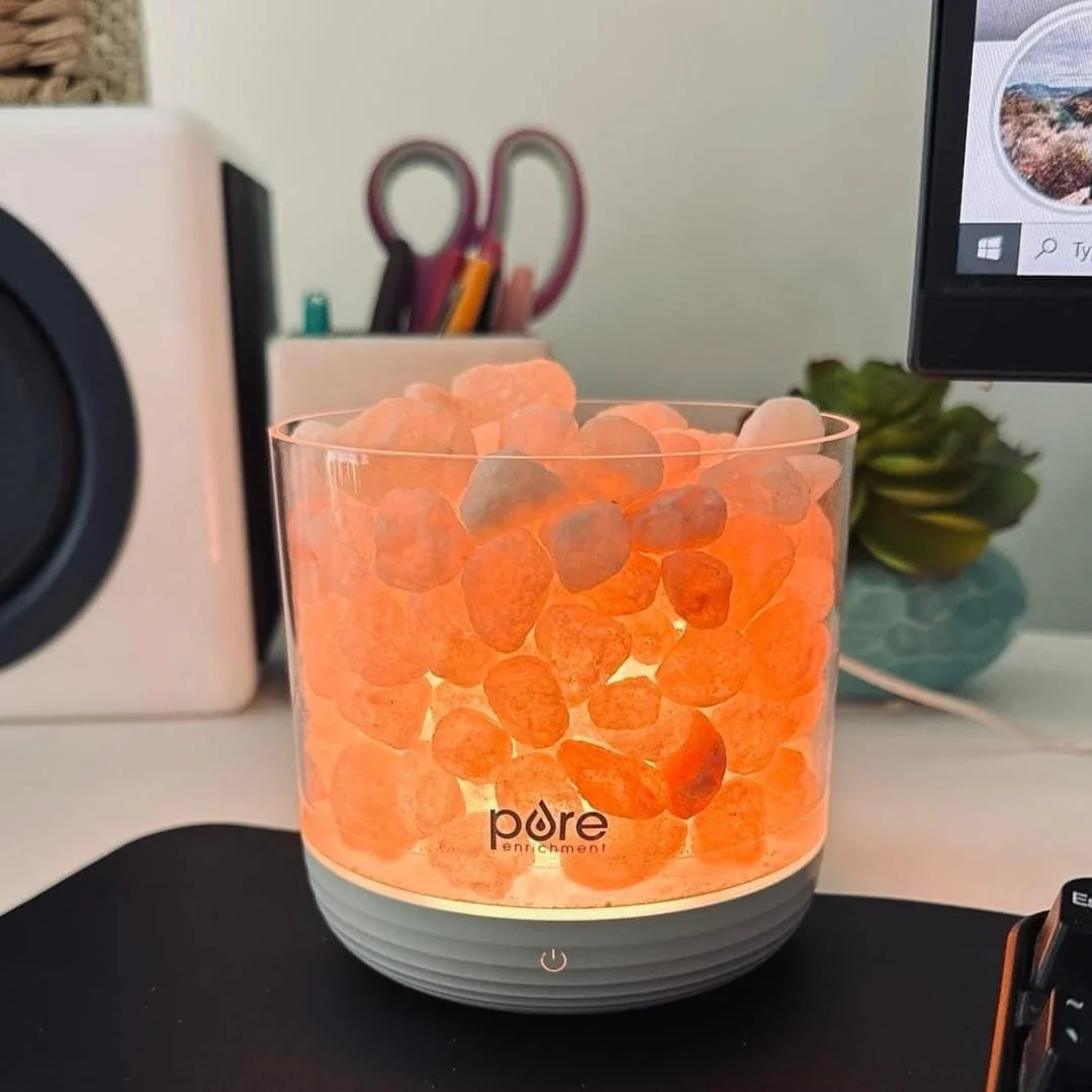Pure Enrichment salt lamp glowing on a desk beside a keyboard and workspace accessories
