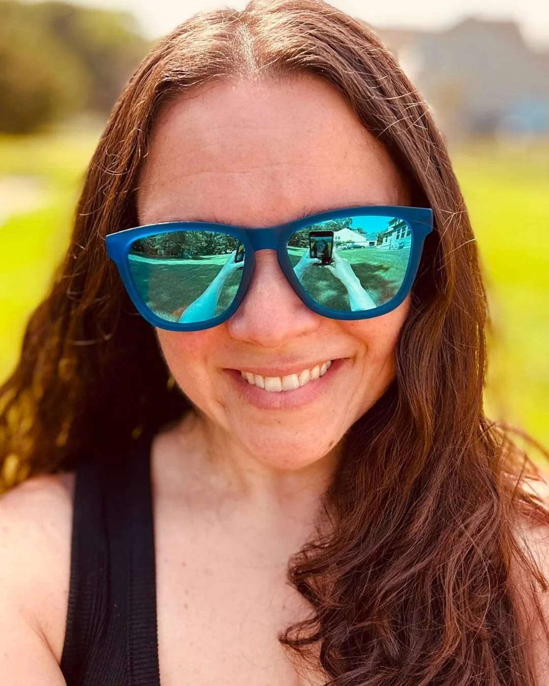 Nicole wearing blue Goodr sunglasses with mirrored lenses reflecting outdoor selfie scene.
