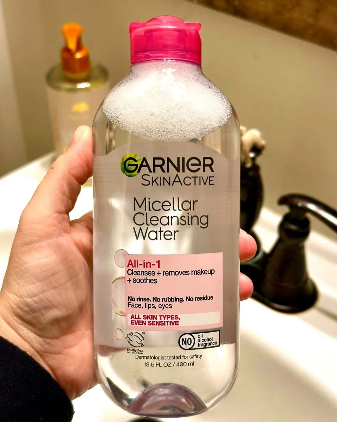 Hand holding a bottle of Garnier SkinActive Micellar Cleansing Water with a pink cap in a bathroom setting
