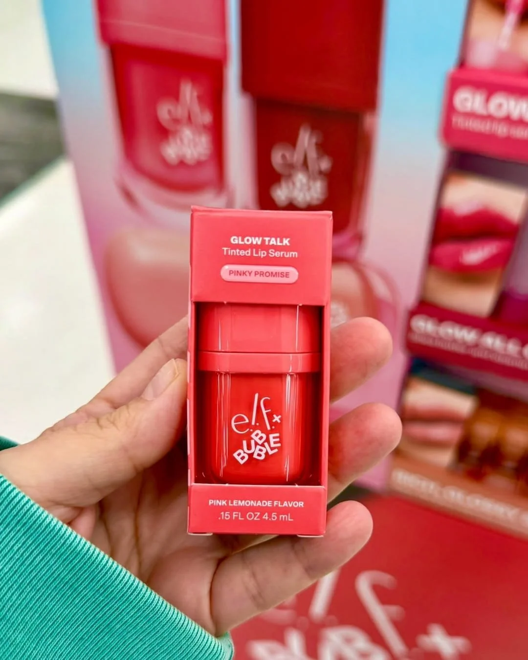 Hand holding e.l.f. x Bubble Glow Talk tinted lip serum in Pinky Promise packaging in a retail beauty display