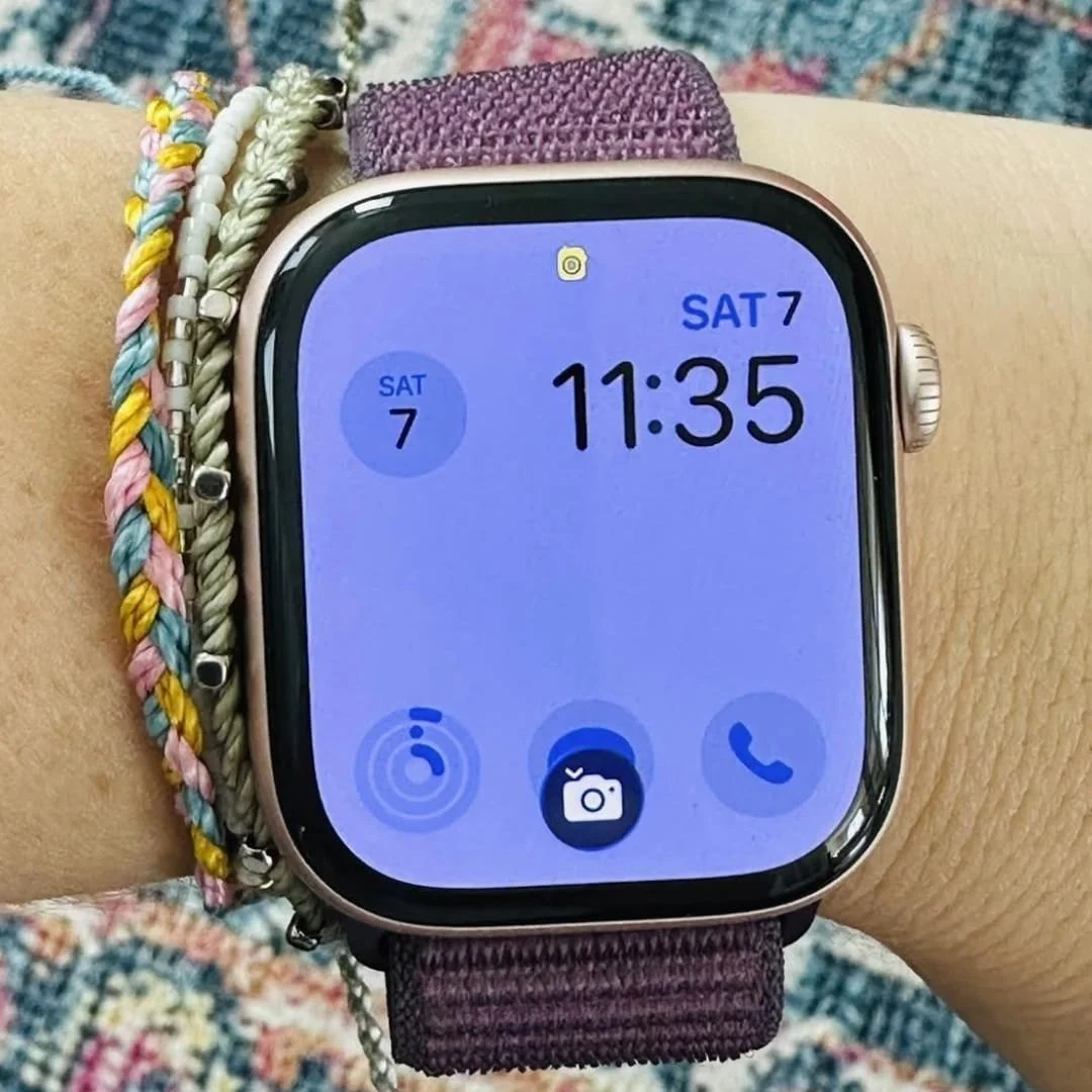 Apple Watch with a purple fabric band displaying the time 11:35 and date SAT 7, accessorized with colorful braided bracelets on the wrist