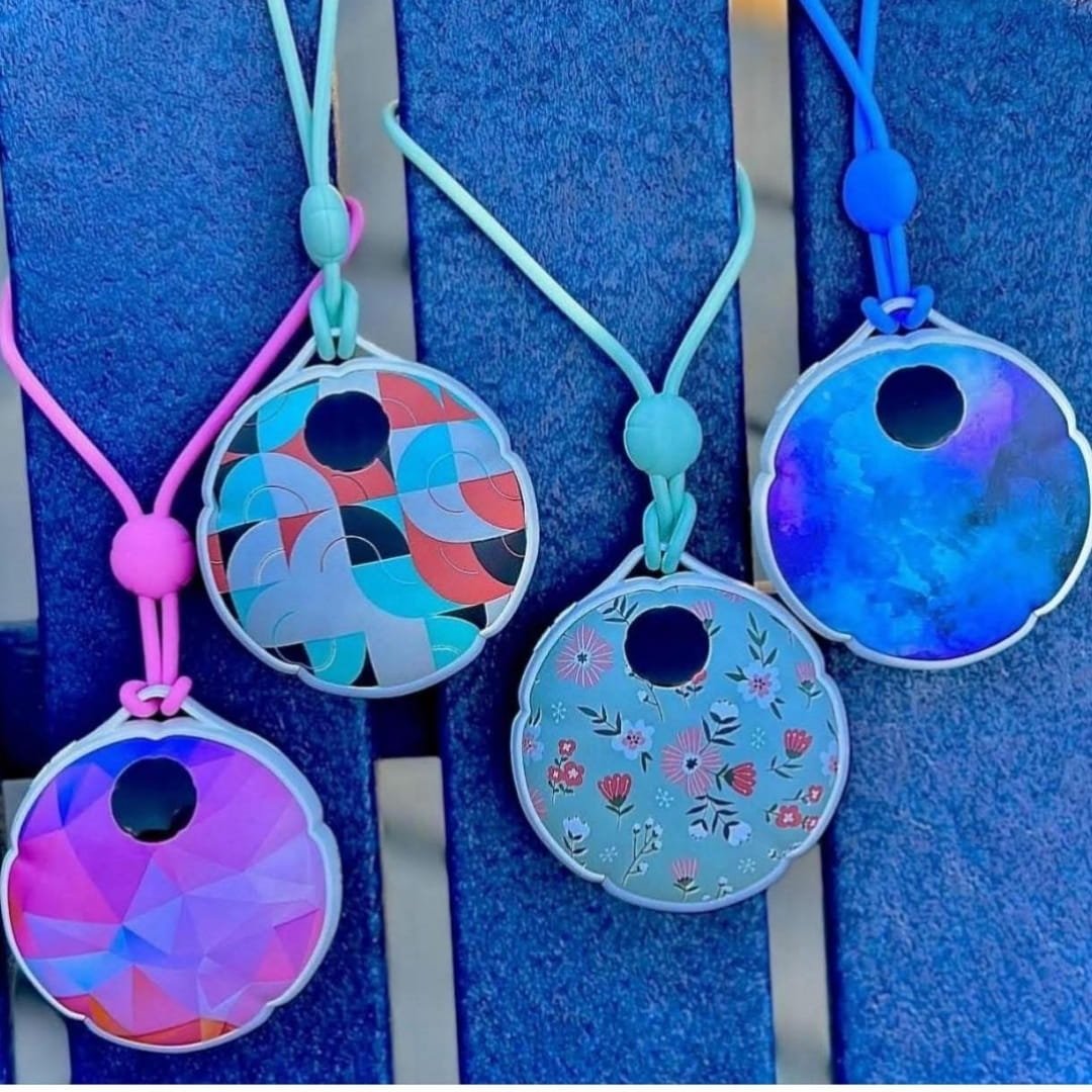 Rechargeable hand warmers with colorful designs, including floral, geometric, and abstract patterns, hanging on pink, teal, and blue cords against a dark blue textured background.