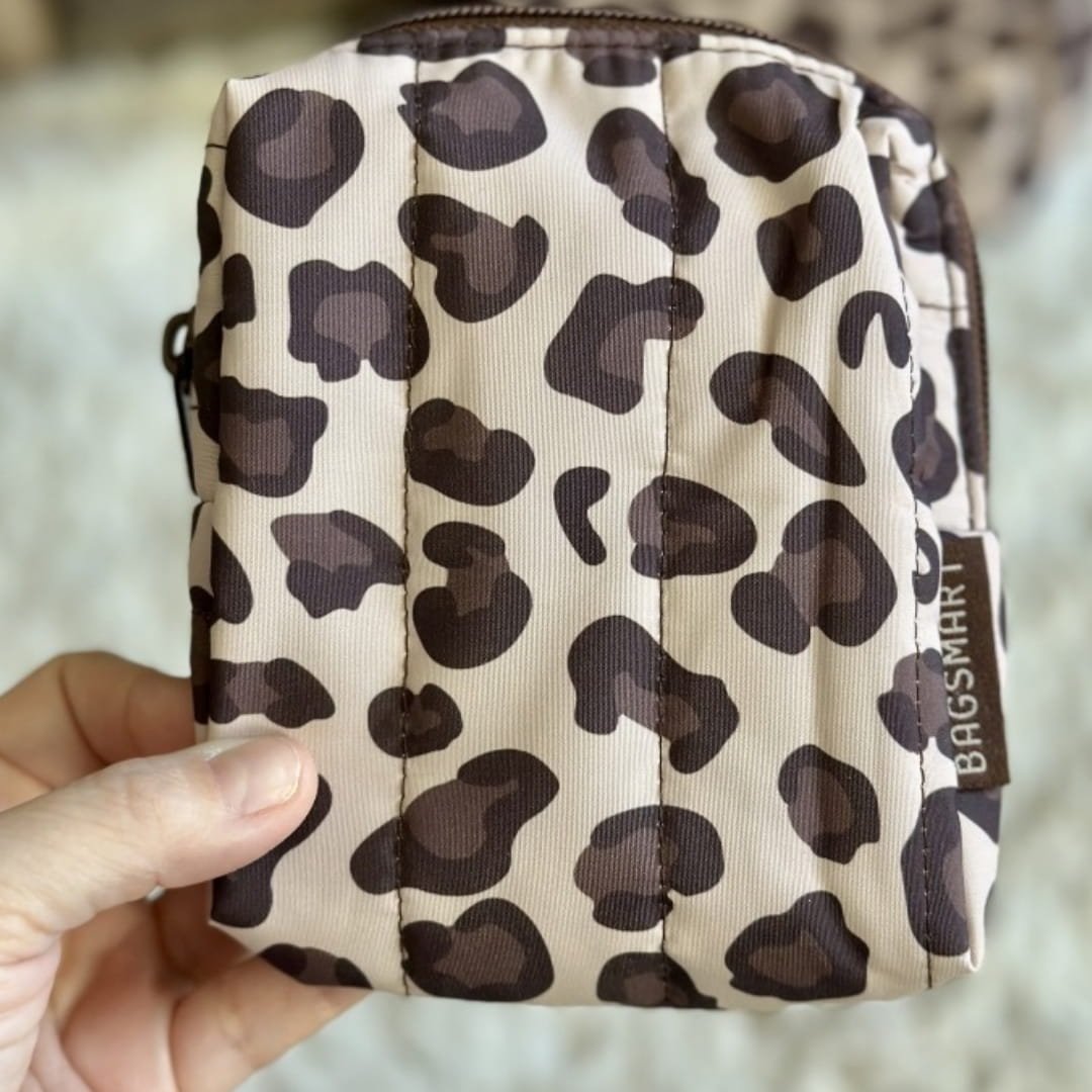 Small quilted leopard-print BAGSMART pouch with brown zipper and branded side tag, held in a hand against a soft white background.