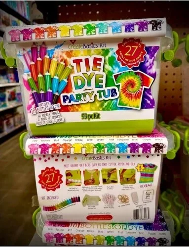 Two stacked CreateBasics Tie Dye Party Tub kits with vibrant labels showcasing 18 dye bottles, rubber bands, gloves, and project guides, displayed on a store shelf.
