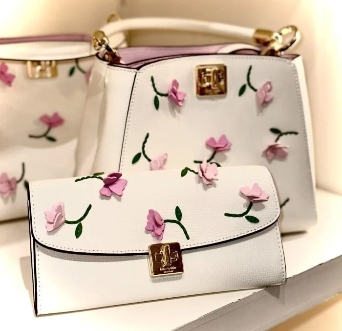 White handbags and wallet with pink floral design and gold accents.