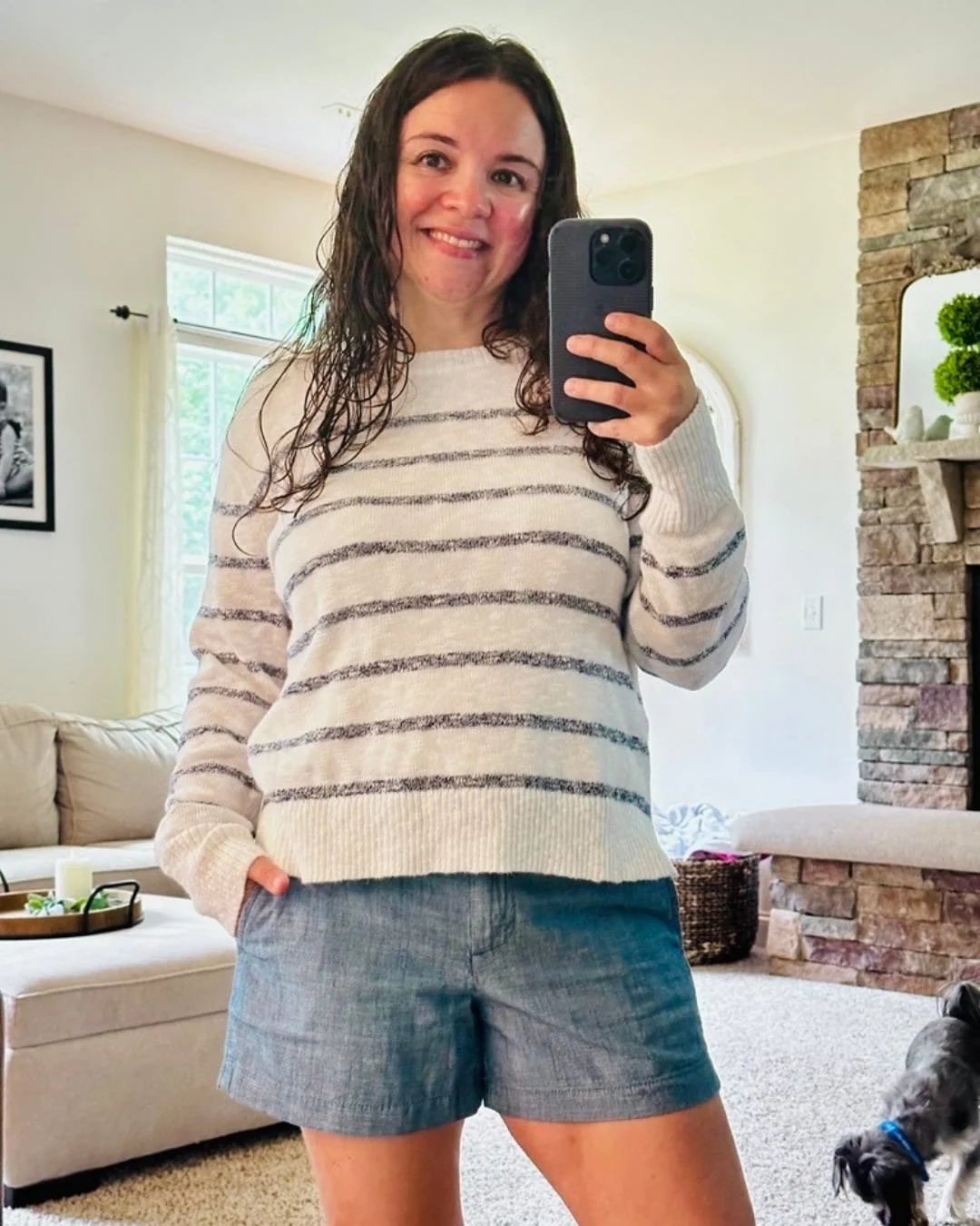 Nicole wearing a striped crewneck sweater with light blue shorts in a living room mirror selfie