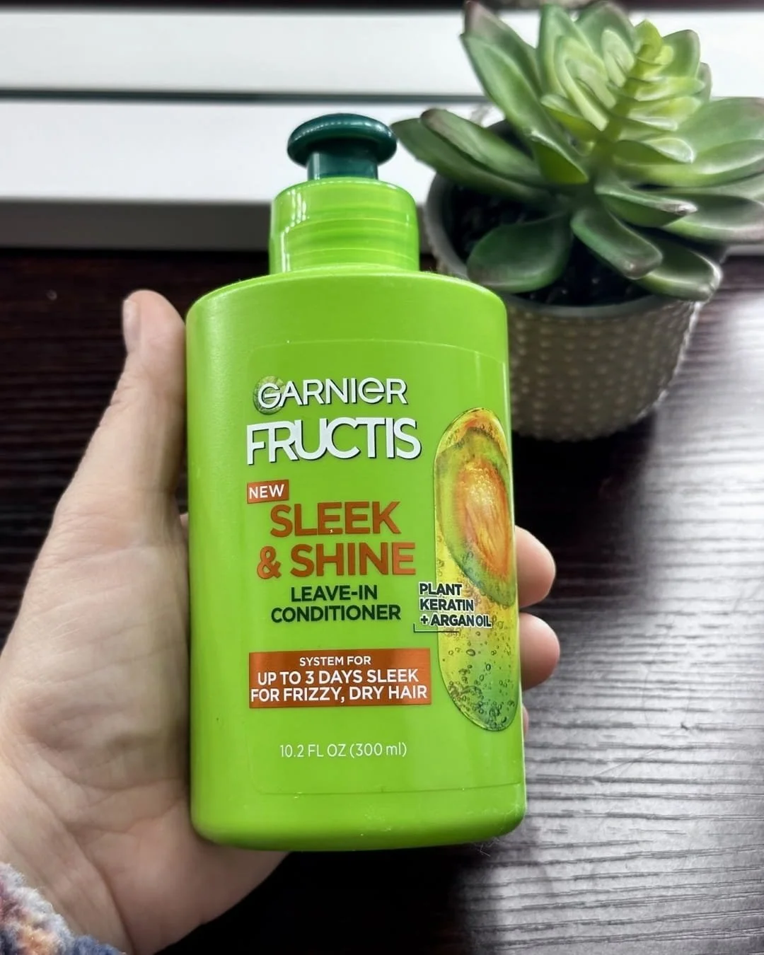 Hand holding Garnier Fructis Sleek and Shine Leave-In Conditioner for frizzy, dry hair with plant keratin and argan oil.