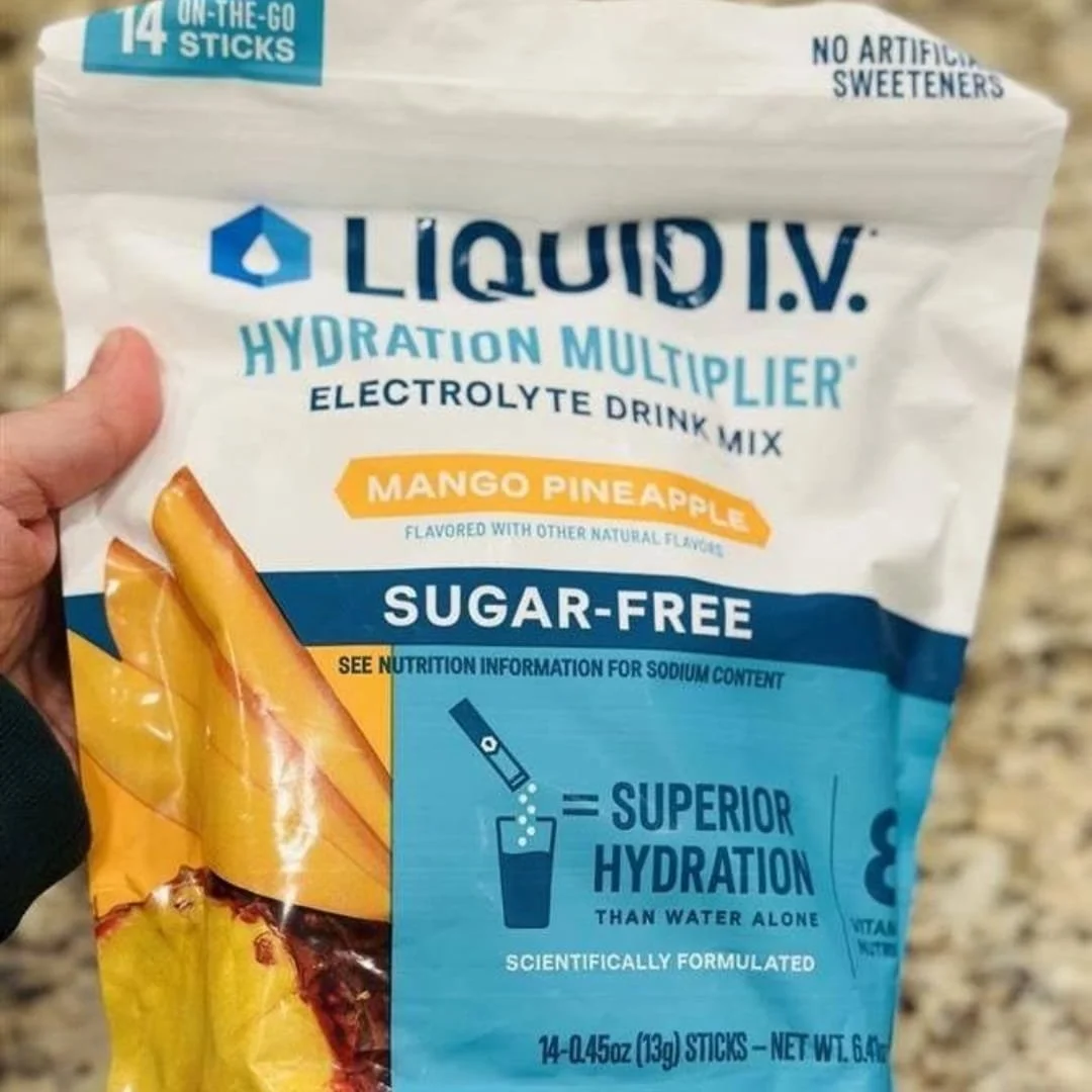 Liquid I.V. Hydration Multiplier in Mango Pineapple flavor, sugar-free electrolyte drink mix with 14 on-the-go sticks, featuring vibrant fruit illustrations and hydration benefits, held over a neutral countertop.