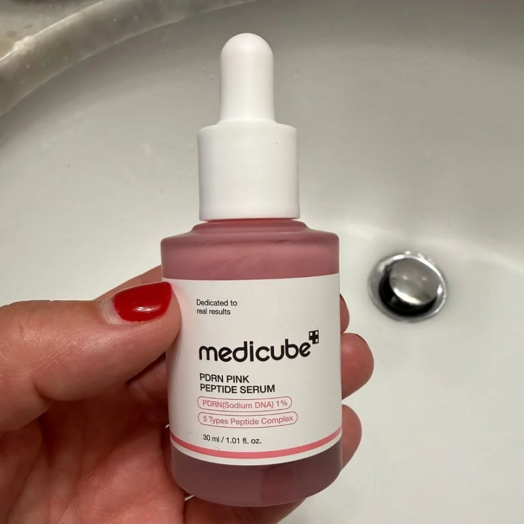 Hand holding a bottle of Medicube PDRN Pink Peptide Serum over a white bathroom sink