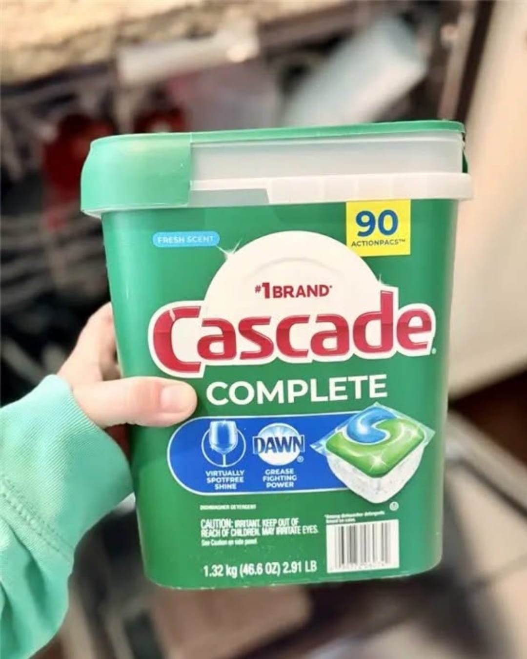 Cascade Complete dishwasher pods container with 90 ActionPacs held in front of open dishwasher