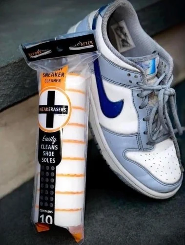 "Packaged SNEAKERASERS instant sneaker cleaner pads displayed next to a clean light blue and white Nike Dunk sneaker on a dark surface.