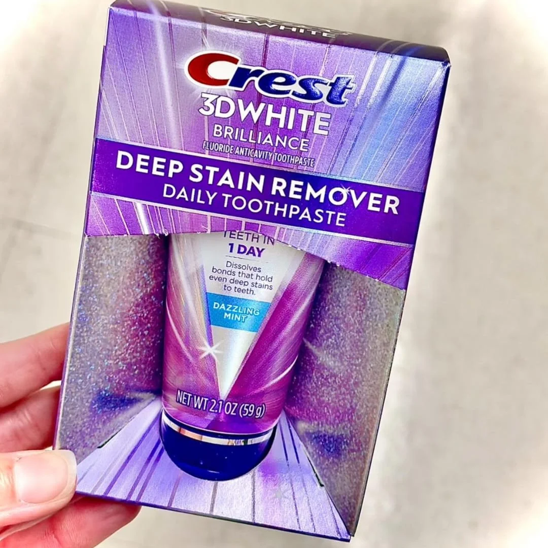 Crest 3D White Brilliance Deep Stain Remover toothpaste in a purple holographic box with a visible tube, highlighting teeth whitening in 1 day and Dazzling Mint flavor.