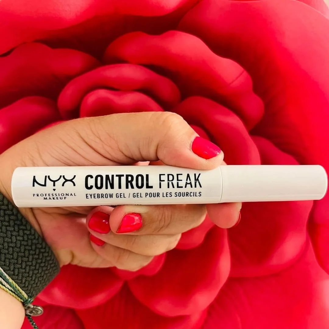 NYX Control Freak eyebrow gel tube held in hand against red rose background