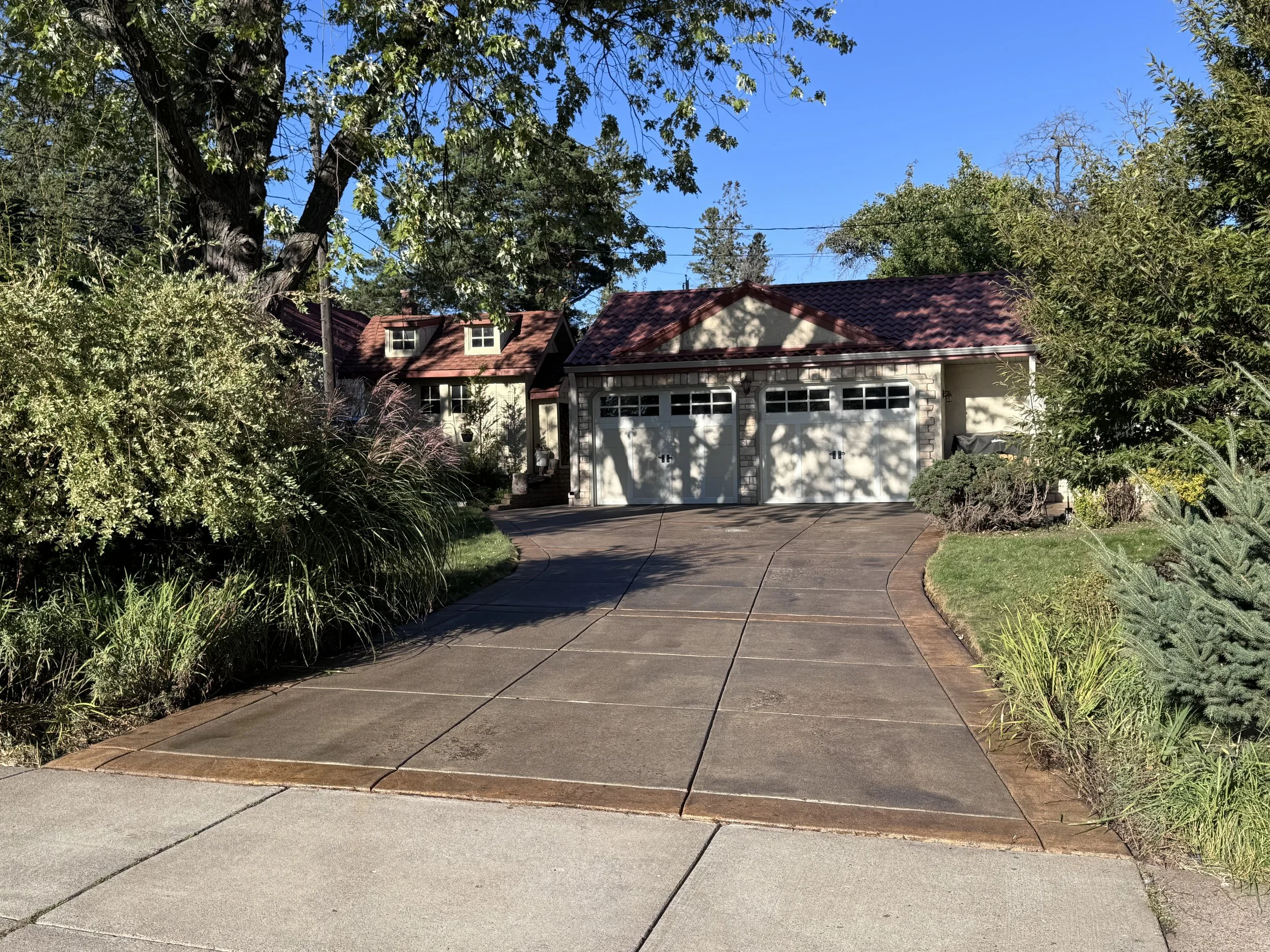 A house with a concrete driveway, garage doors, trees, and landscaping.
