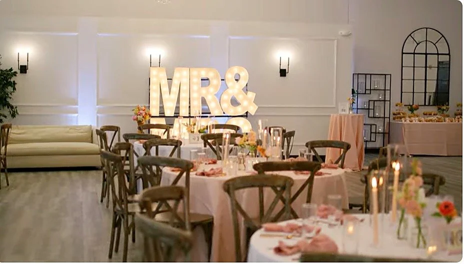 Wedding reception at LedgeCrest Reserve with lit "Mr & Mrs" marquee sign, round tables, and candlelit place settings
