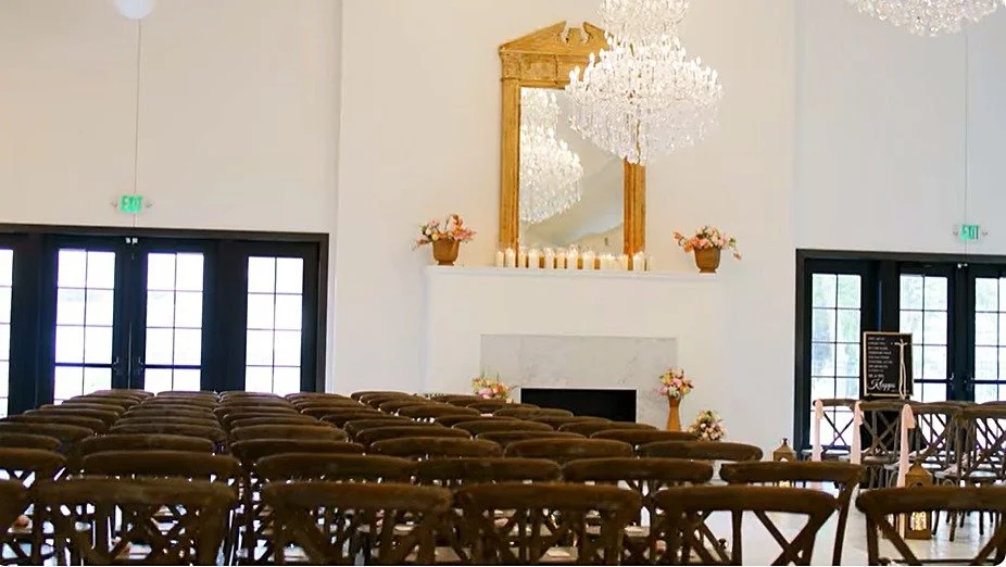 Indoor wedding ceremony setup at LedgeCrest Reserve with crystal chandeliers, gold-framed mirror, and rows of wooden cross-back chairs