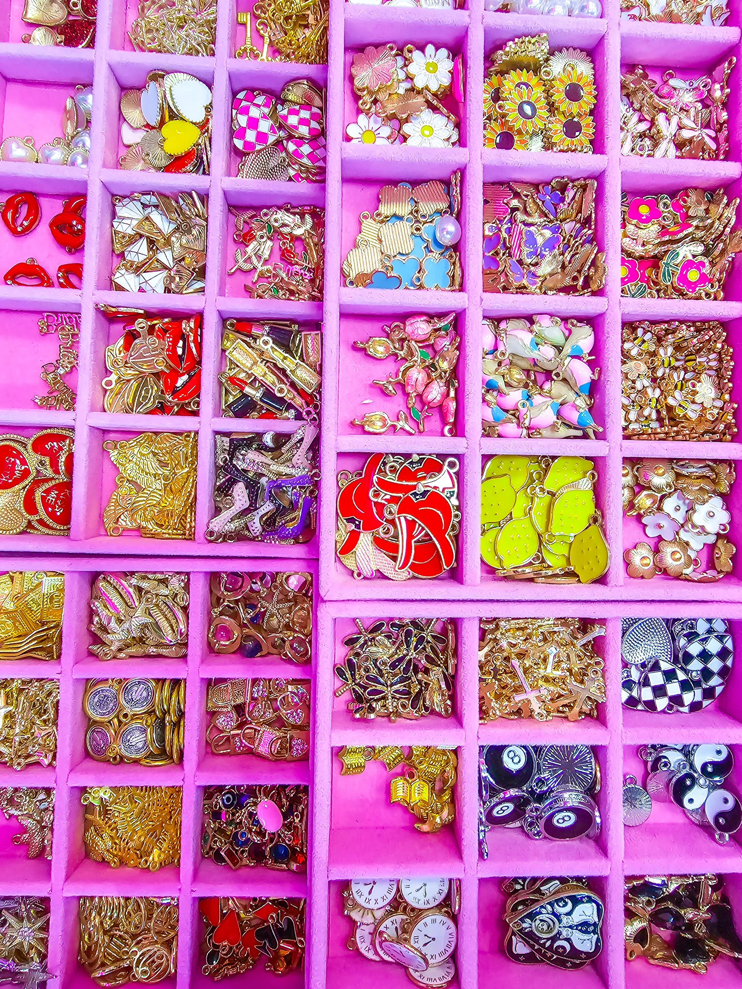 Plastic pink organizer box filled with assorted colorful jewelry charms, pendants, and trinkets.