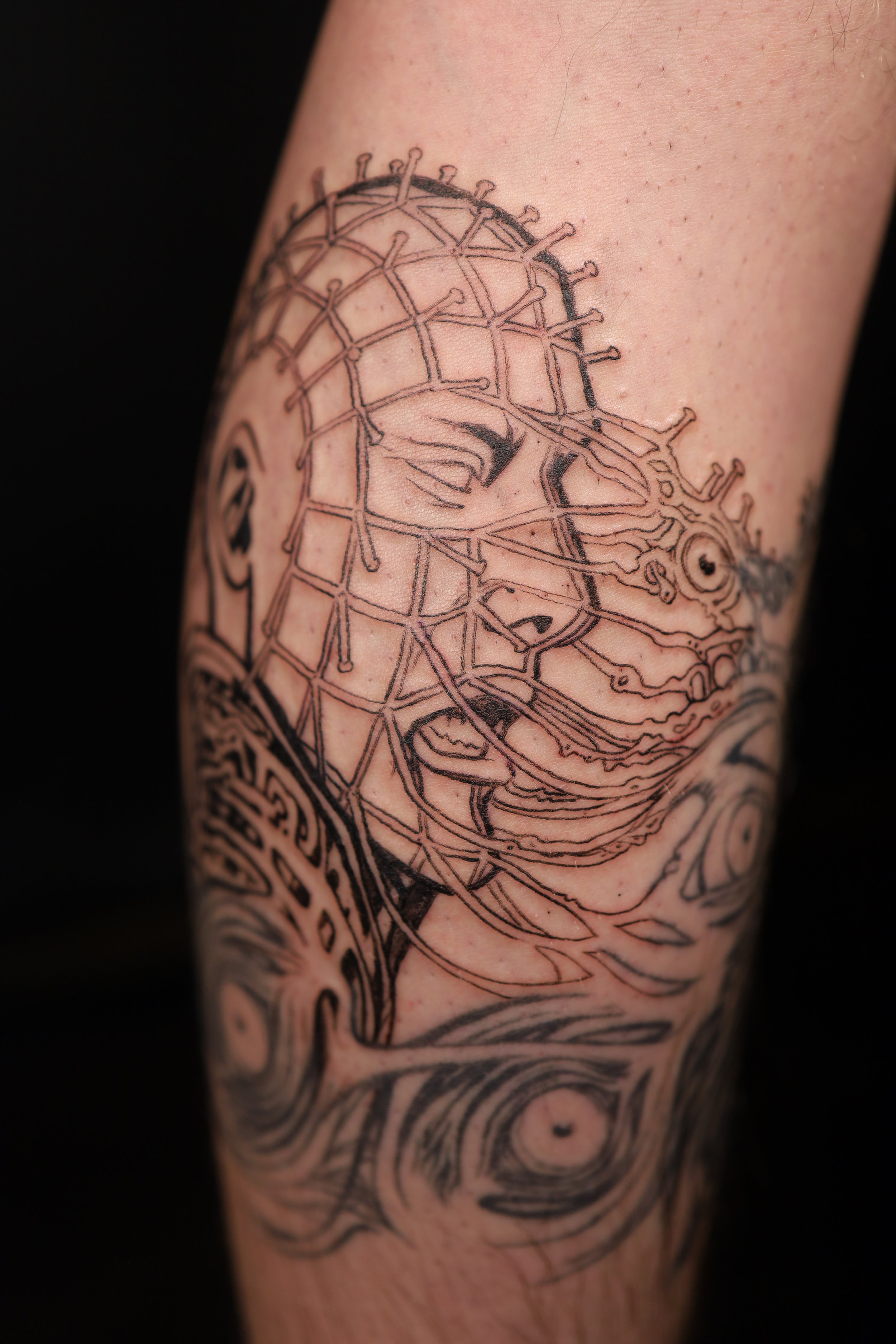 Tattoo of a woman's face with closed eyes, surrounded by abstract lines and elements, on a person's arm.
