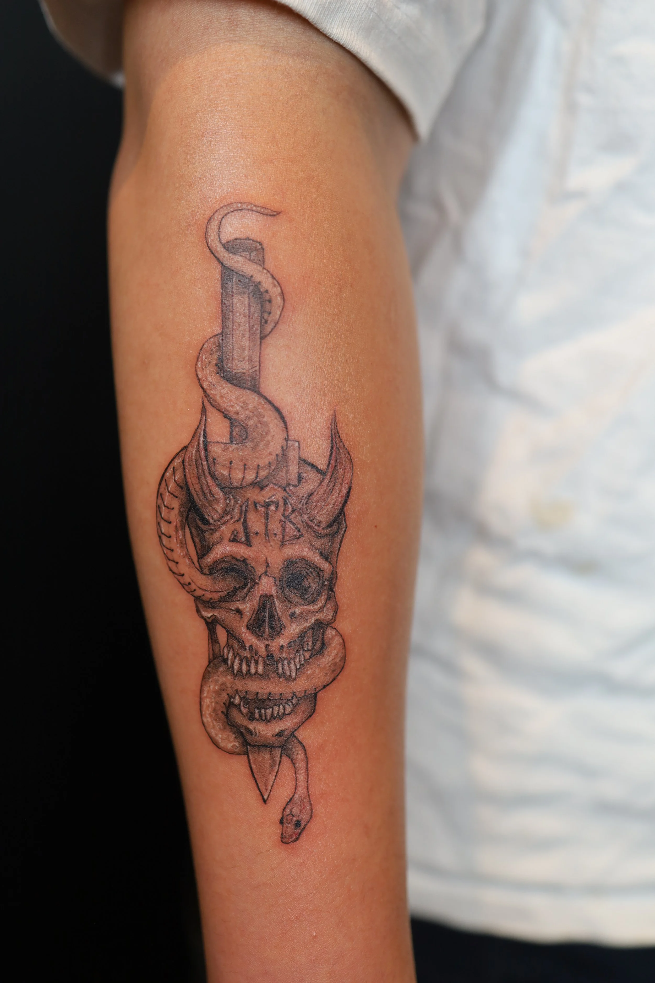 Tattoo of a skull with horns intertwined with a snake on a person's arm.