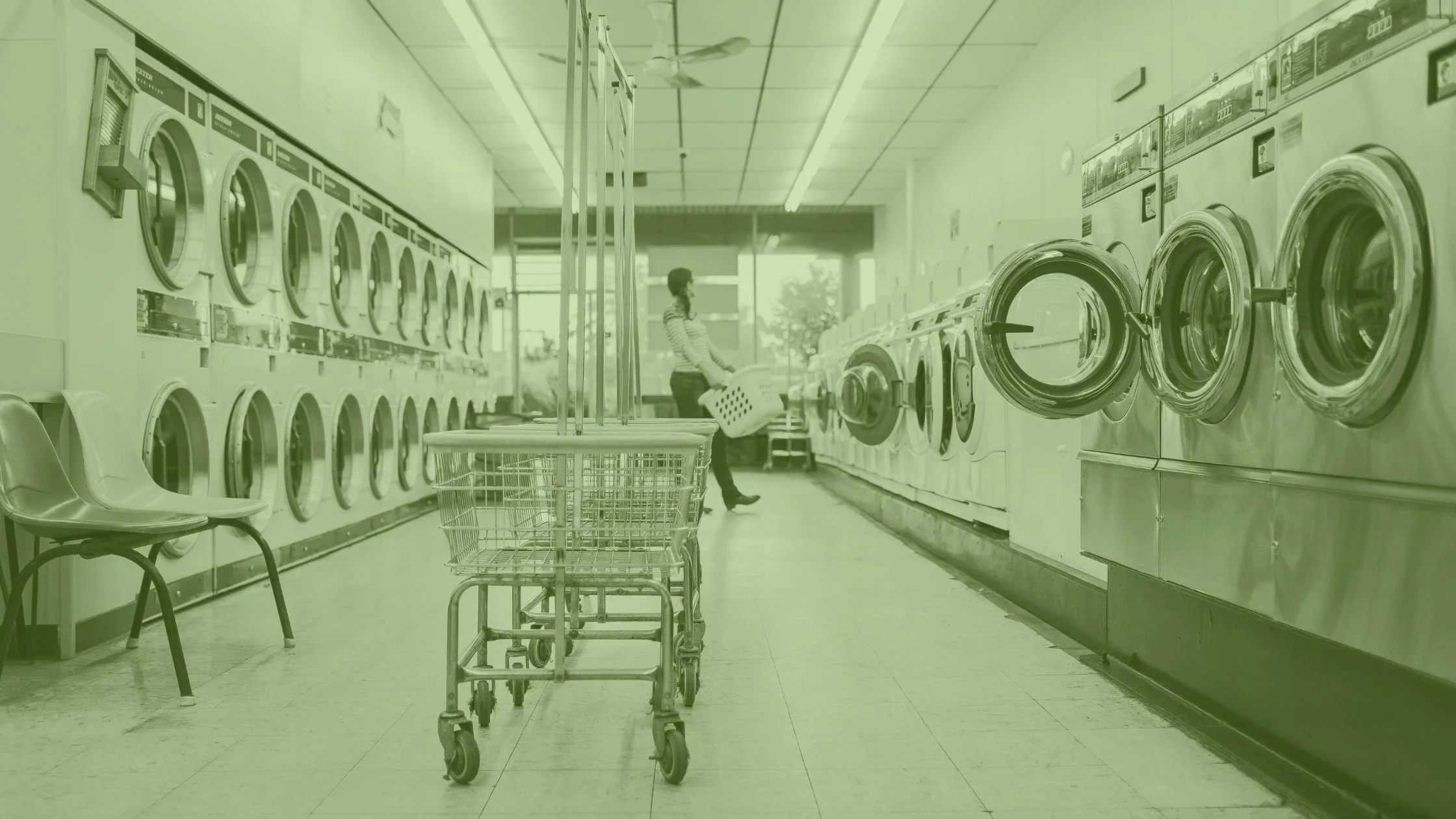 Wide-angle view of a laundromat aisle filled with used commercial laundry equipment, including front-load washers with aging exteriors and coin mechanisms.