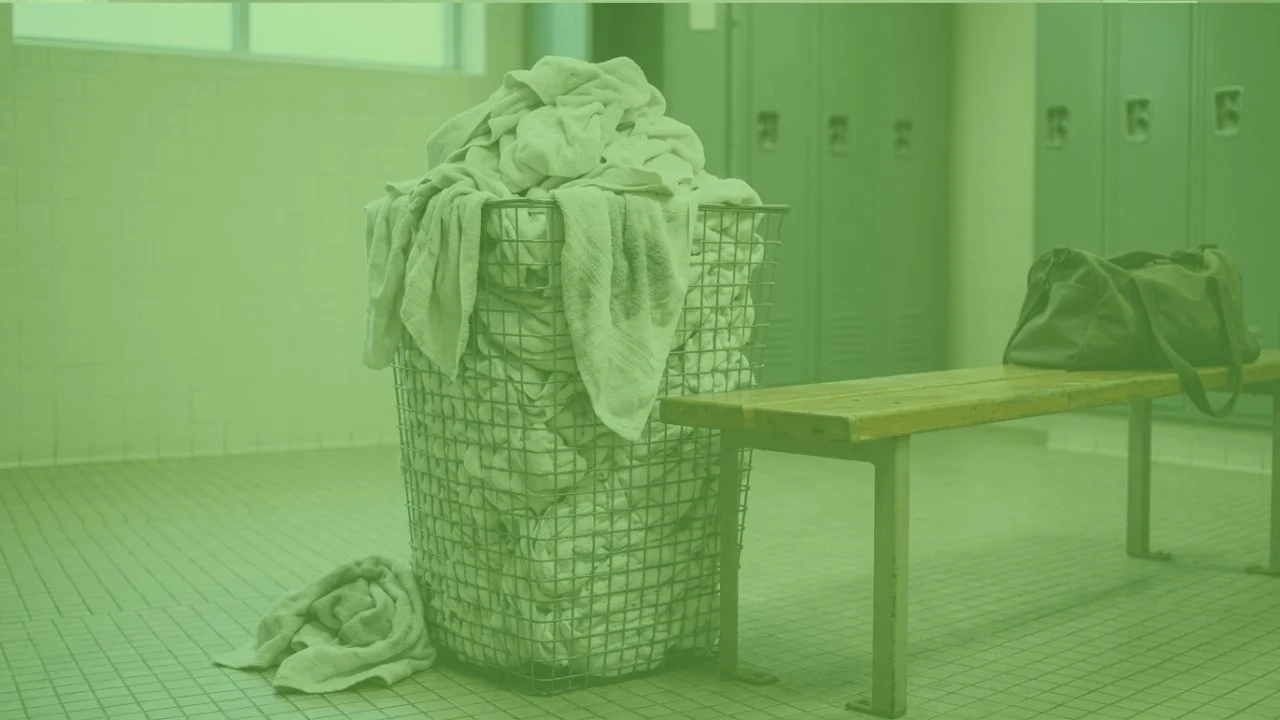 Damp used towels piled in a locker room bin, the starting point of gym towel odor before laundry