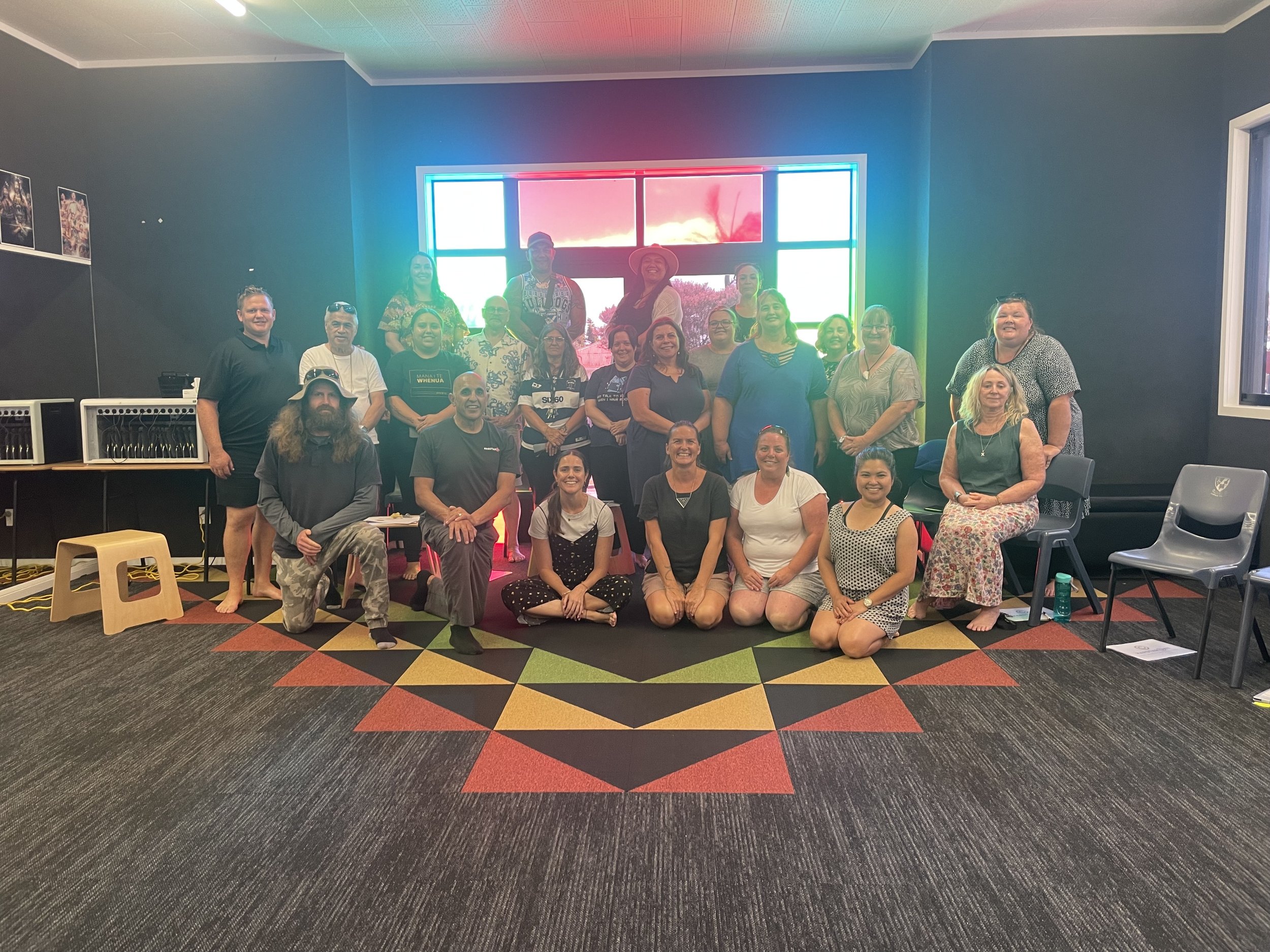 Group of teachers smiling in a room with a colourful neon-lit window and a patterned carpet.