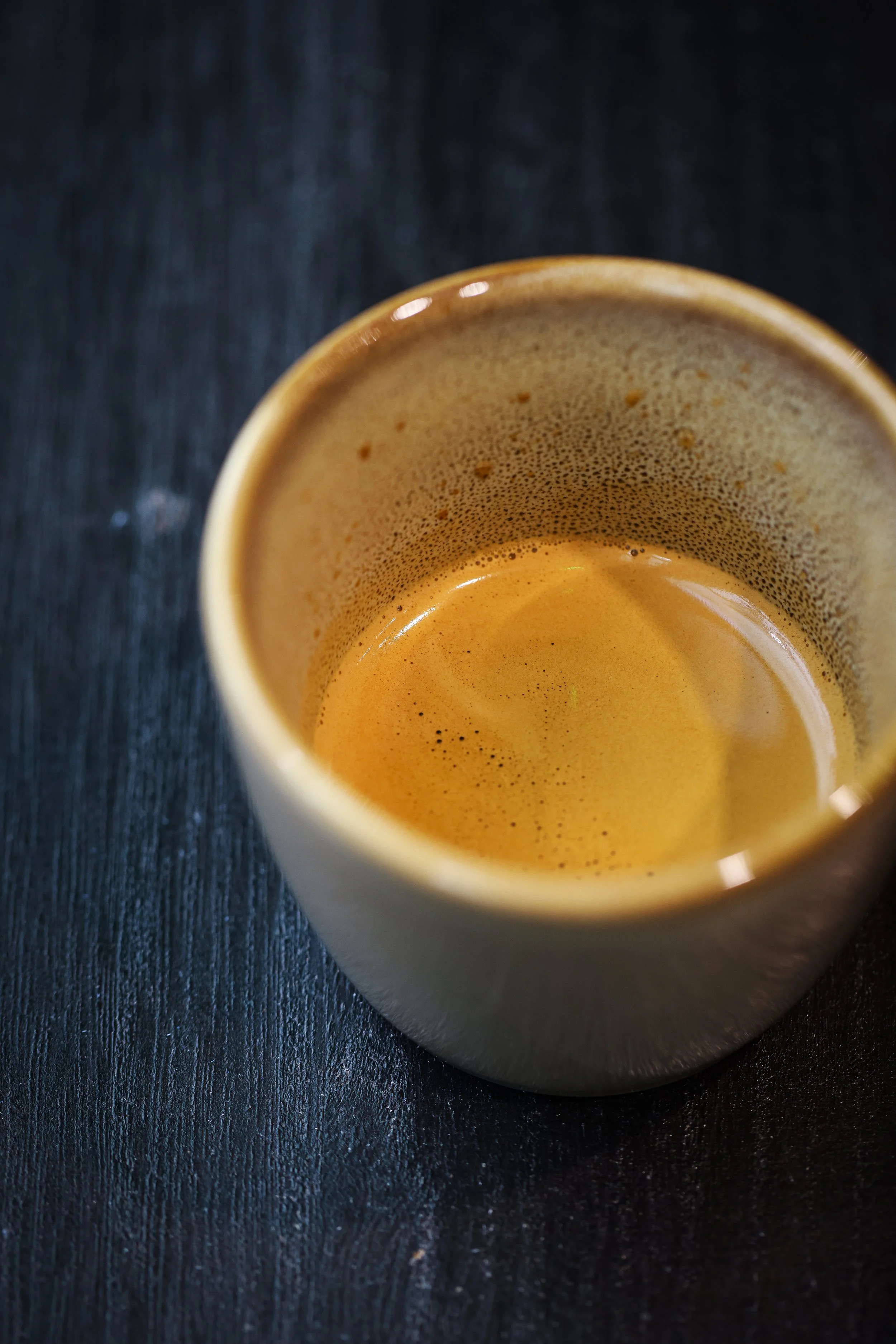 Close-up of a ceramic cup with freshly brewed espresso against a dark textured background.