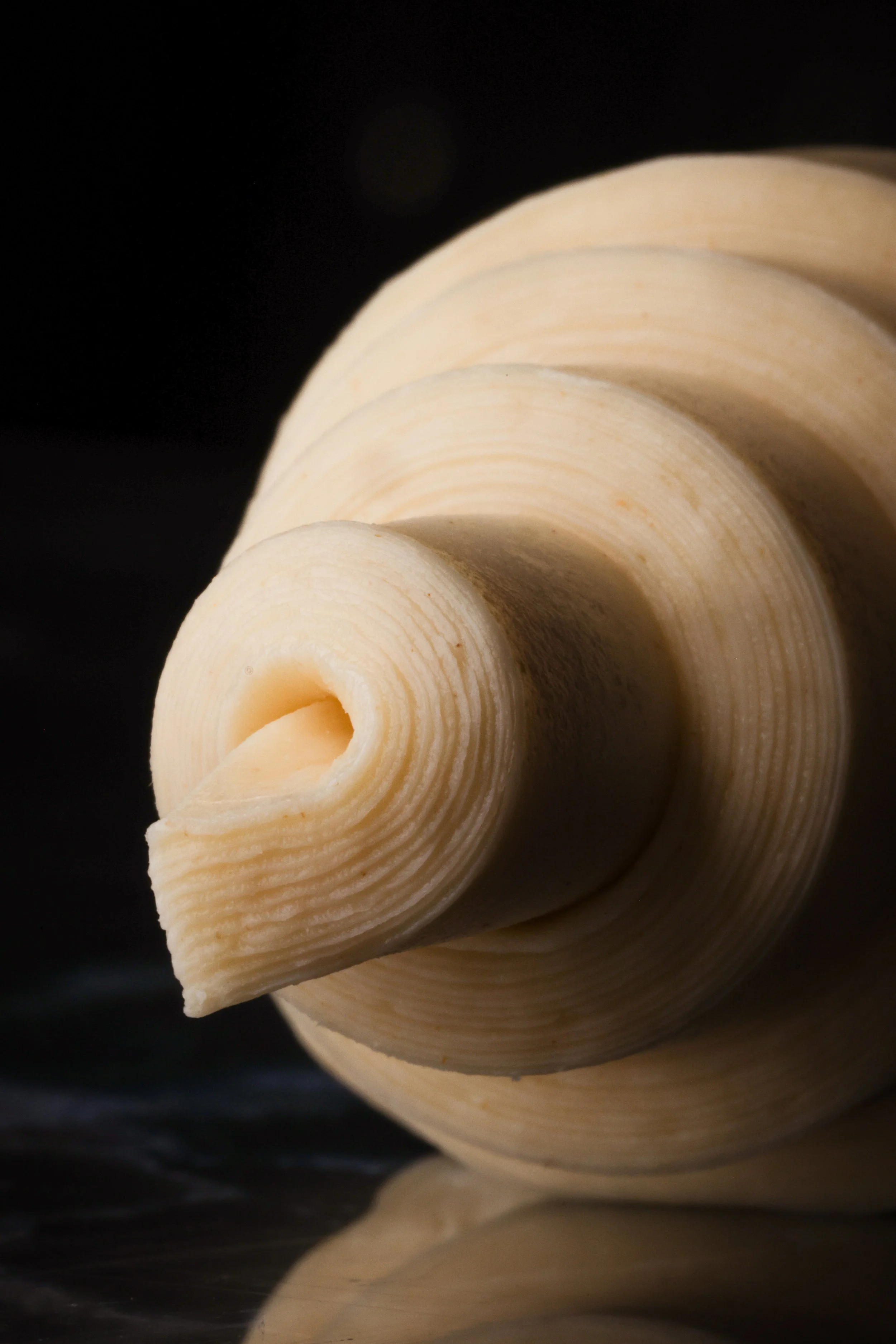 Close-up of a curled butter curl on a reflective surface with a dark background.