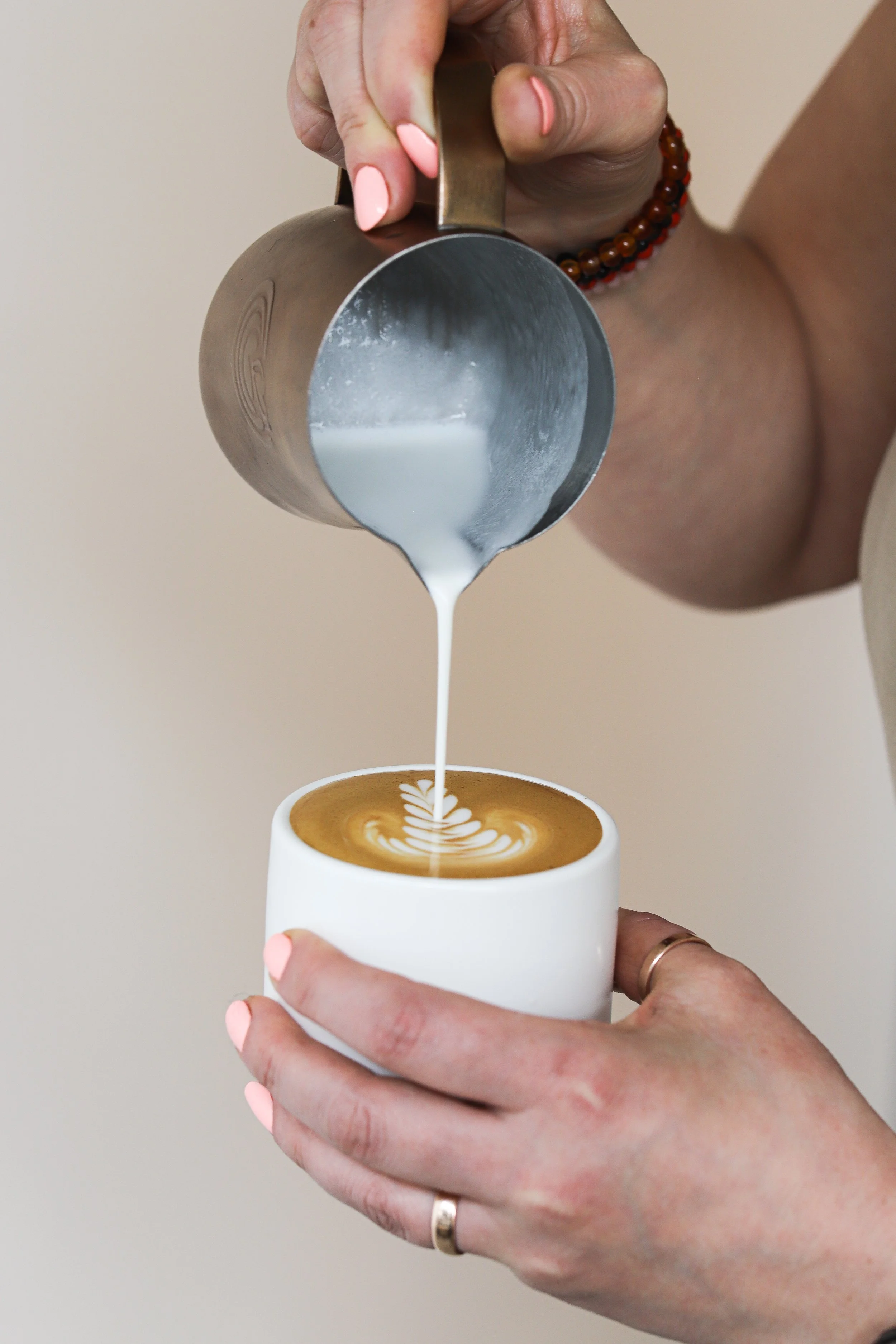 Close-up of a person pouring steamed milk into a cup of coffee, creating latte art.