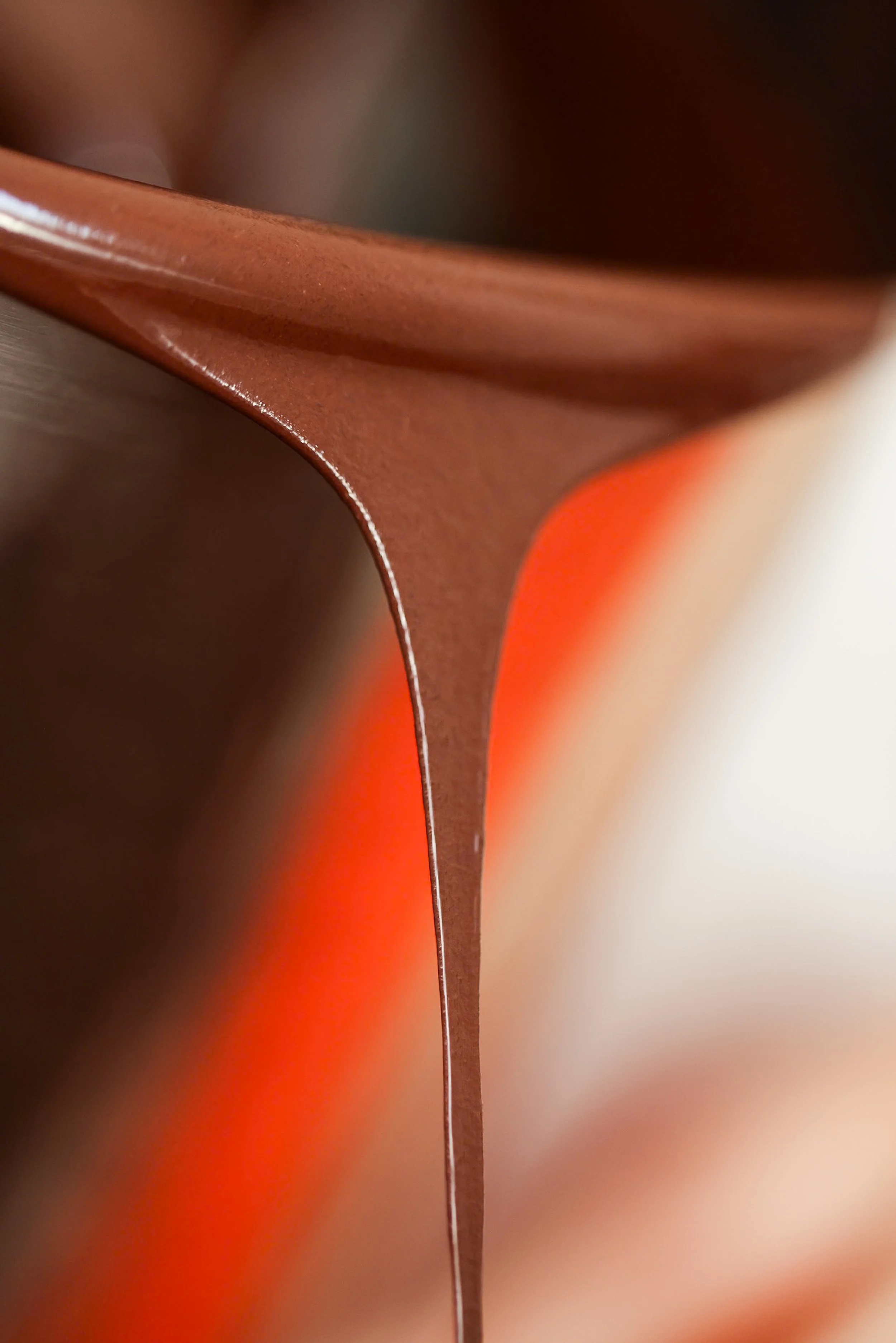A person holding a glass cup of yogurt parfait with granola, layered with white yogurt and topped with berry sauce and sliced almonds. The parfait is on a green plate with a napkin beside it.