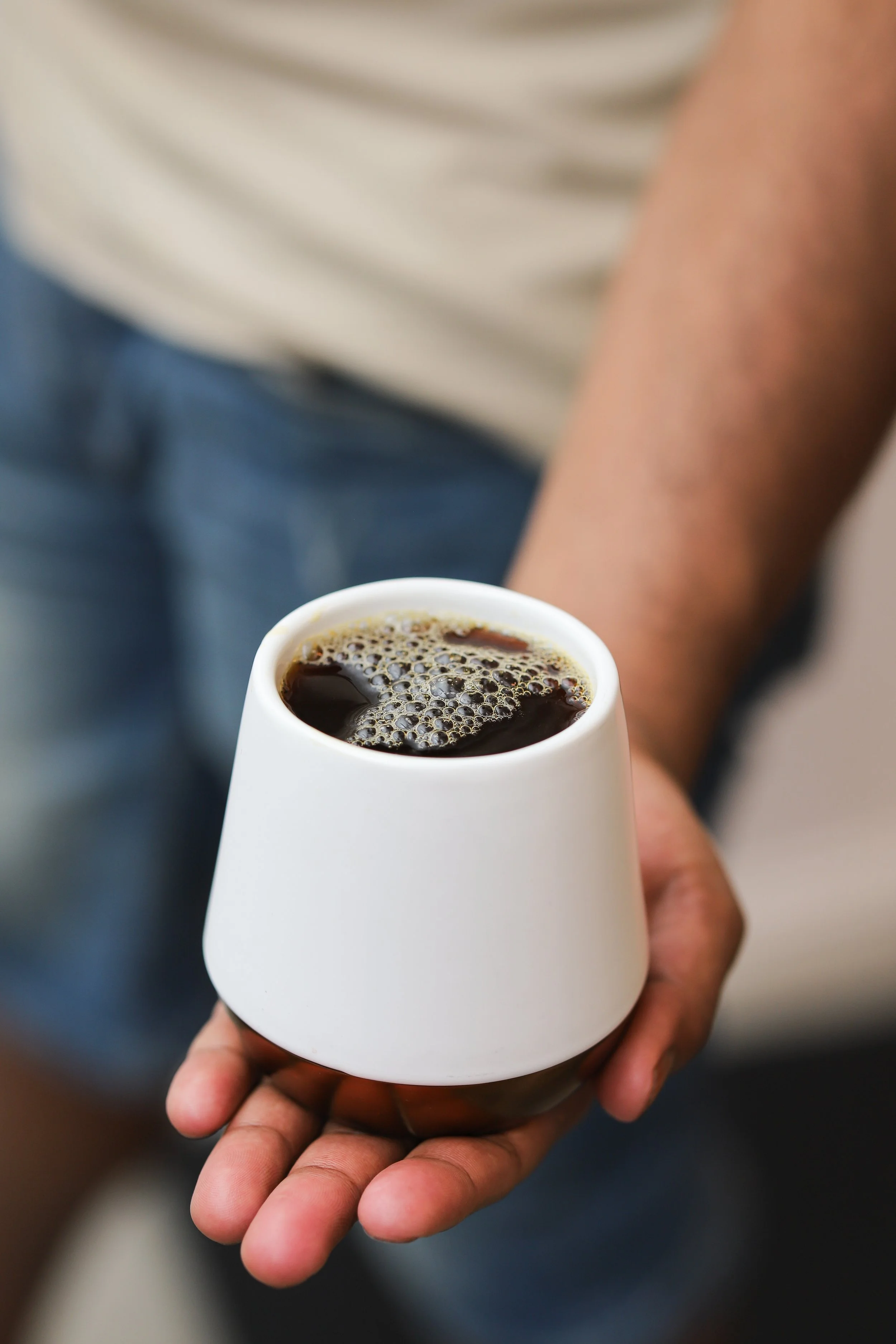 A person holding a white cup filled with black coffee.