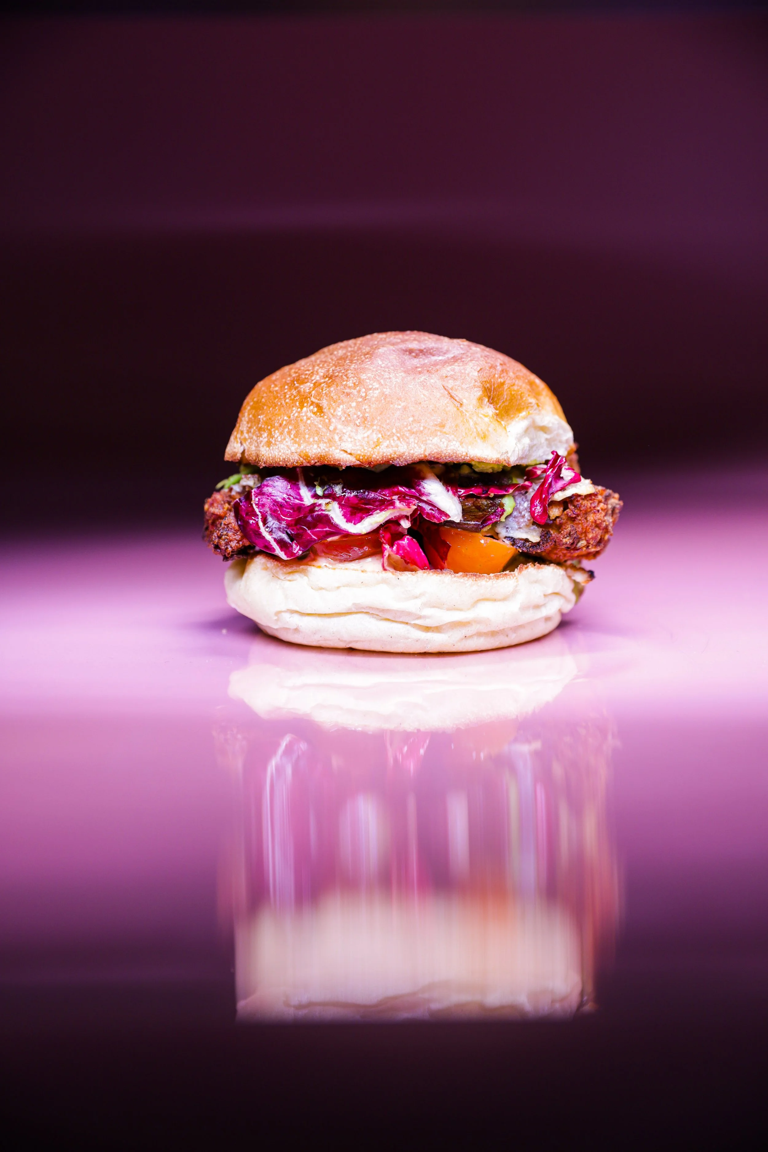 Gourmet chicken sandwich with lettuce and tomato on a glossy pink background.