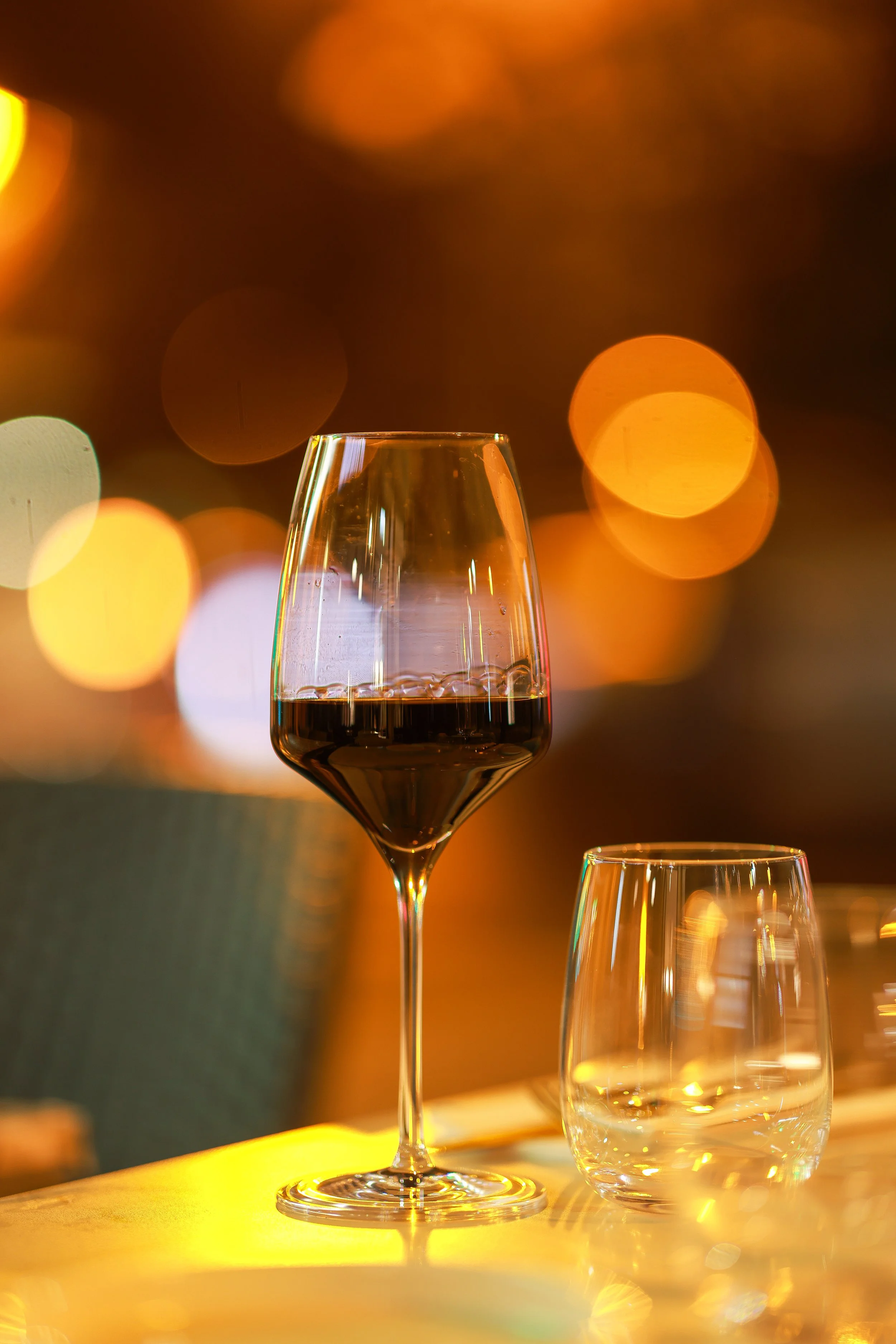 Wine glass with red wine on a table, empty glass nearby, warm bokeh background