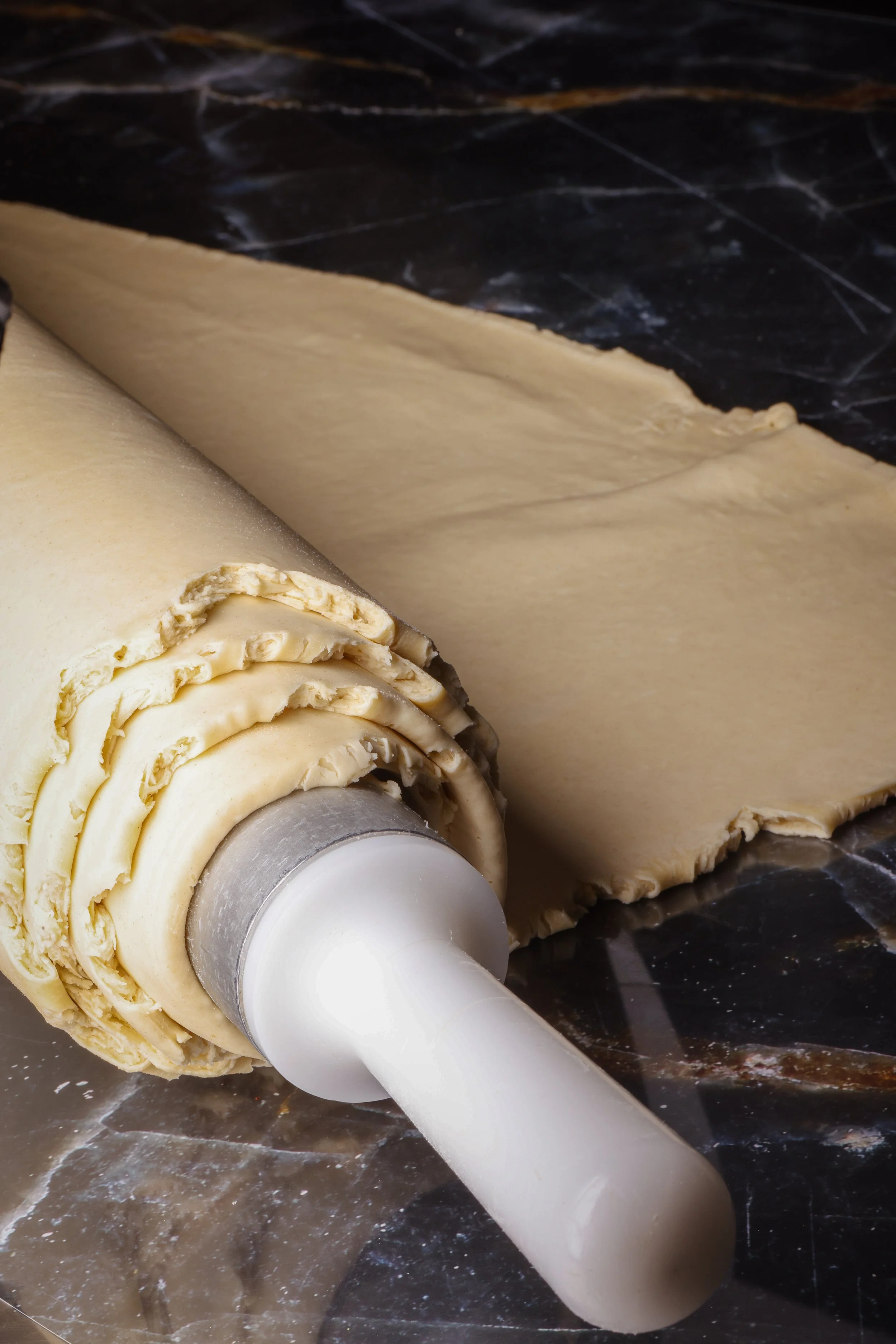 Rolling pin with rolled-out dough on a dark marble surface.