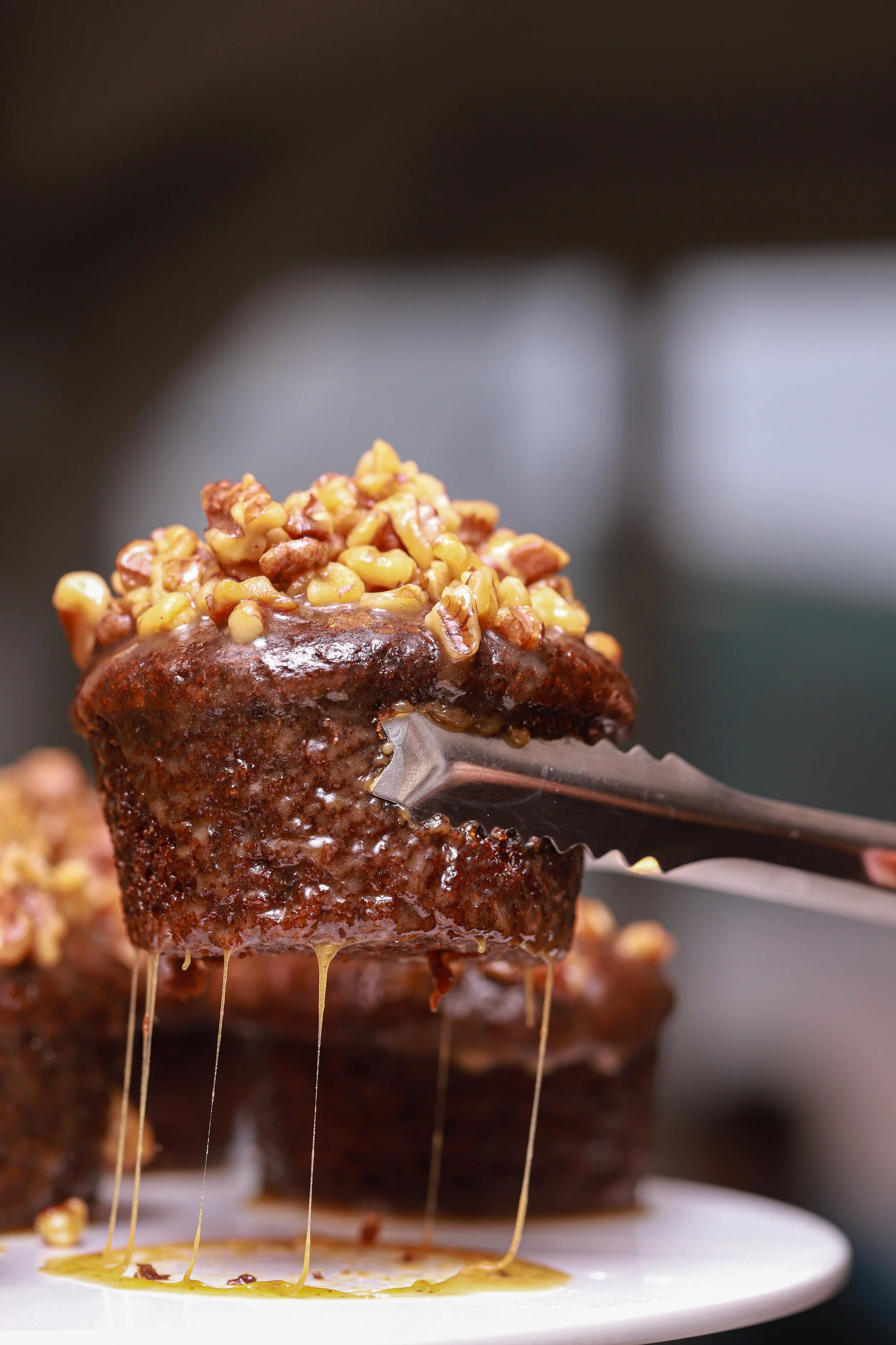Close-up of a pecan-topped sticky bun being lifted with tongs, with honey dripping from it.
