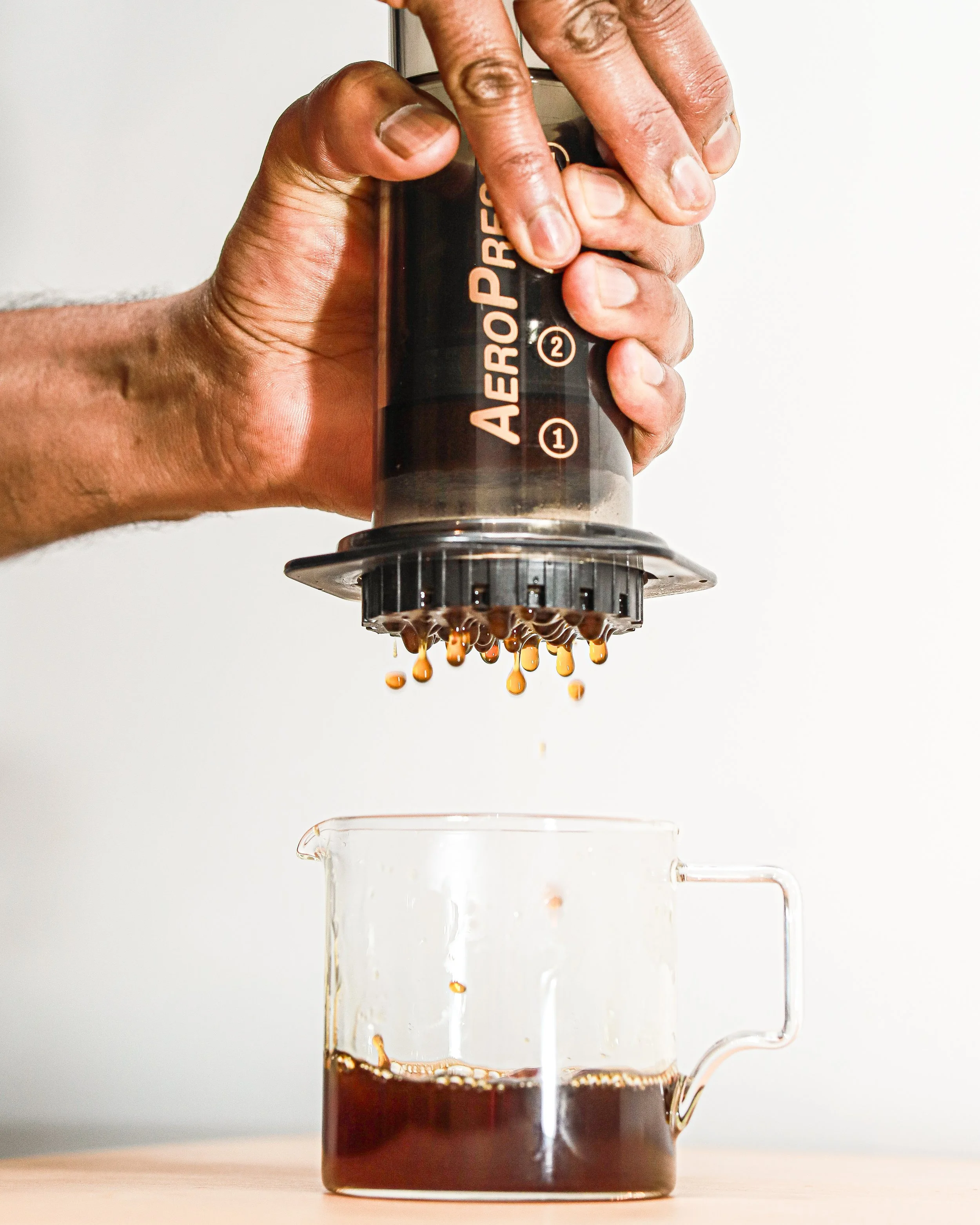Person using AeroPress coffee maker to brew coffee into a glass mug.