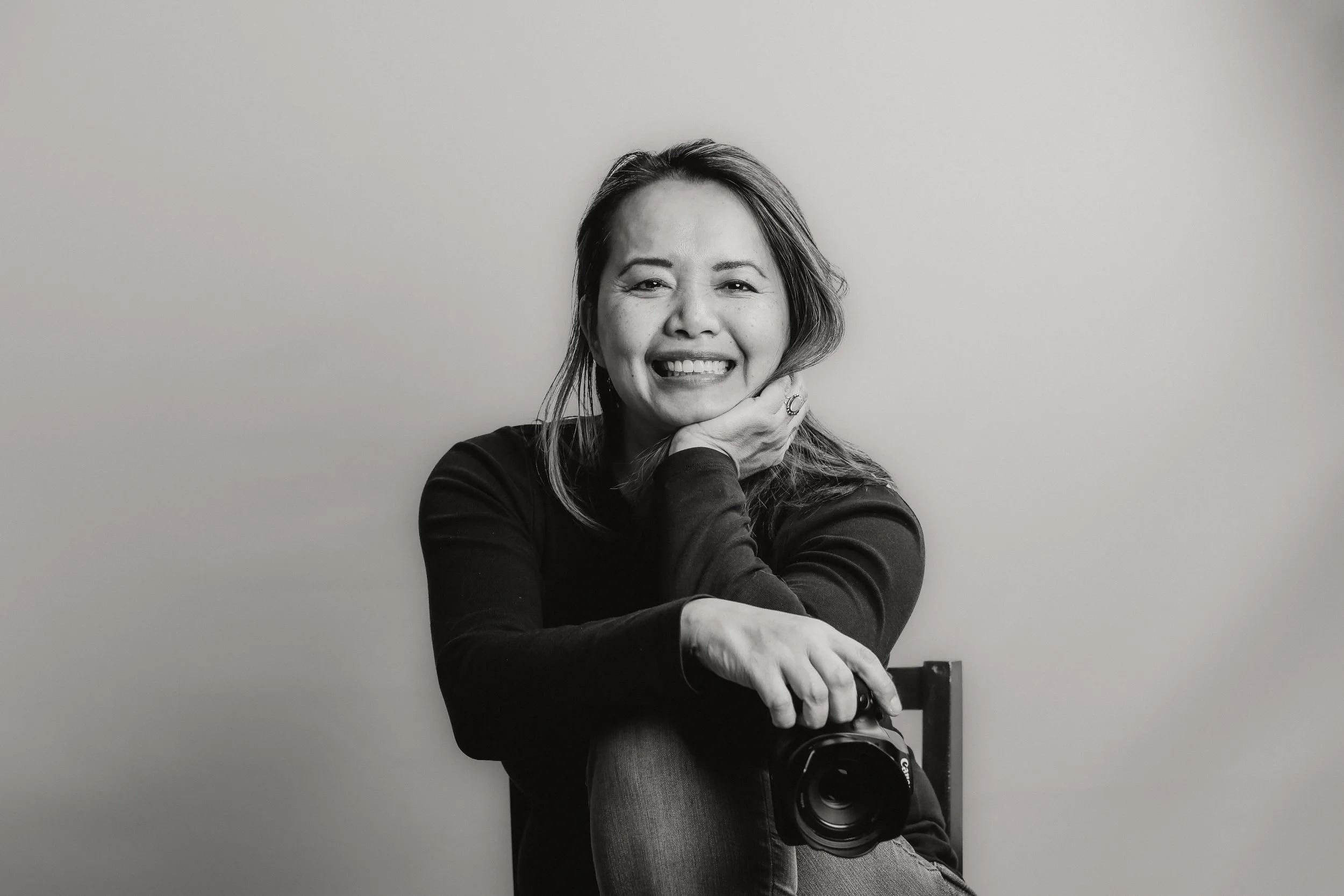 Smiling woman seated with a camera, monochrome.