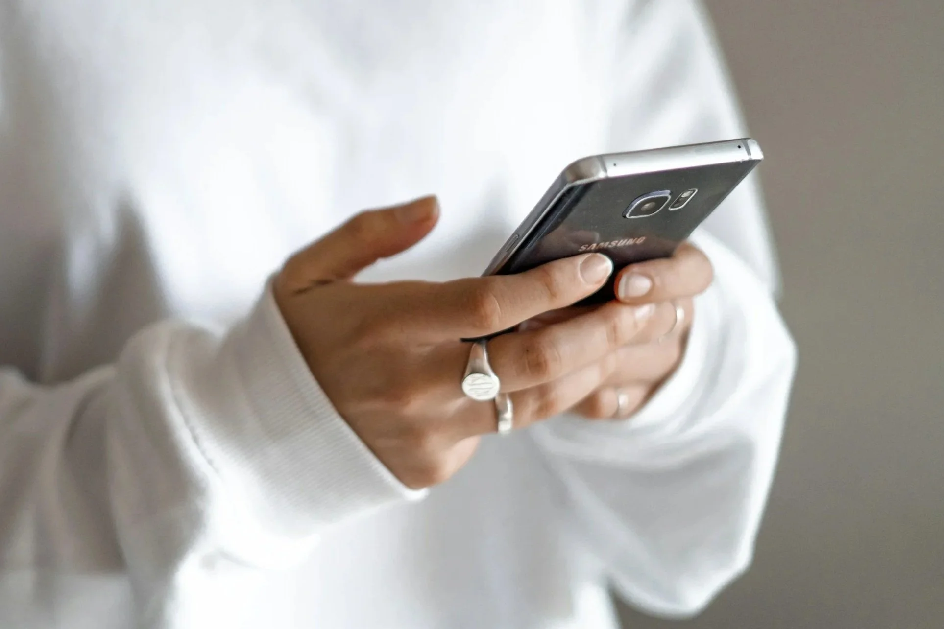 Person holding a Samsung smartphone, wearing a white long-sleeve shirt and silver rings.