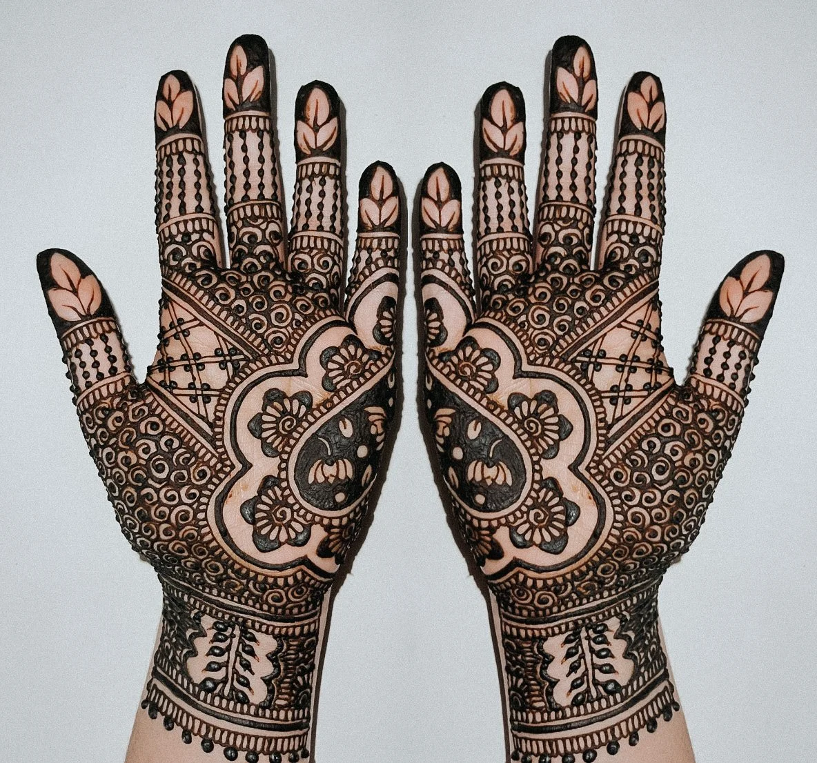 Two hands with intricate henna or mehndi designs in black ink on the palms and fingers, featuring floral and geometric patterns.