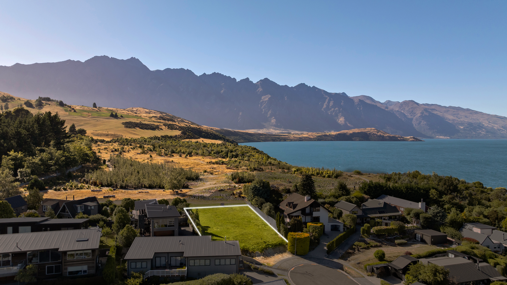 Aerial view of a residential neighborhood next to a large lake with mountains in the background under a clear blue sky.