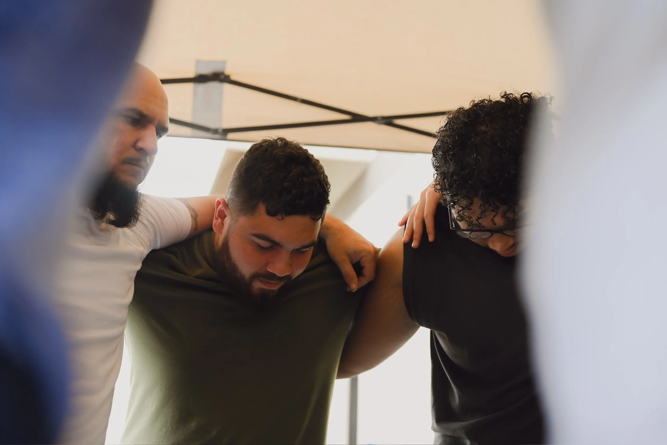Three men in a close circle with heads bowed, showing unity and solidarity.