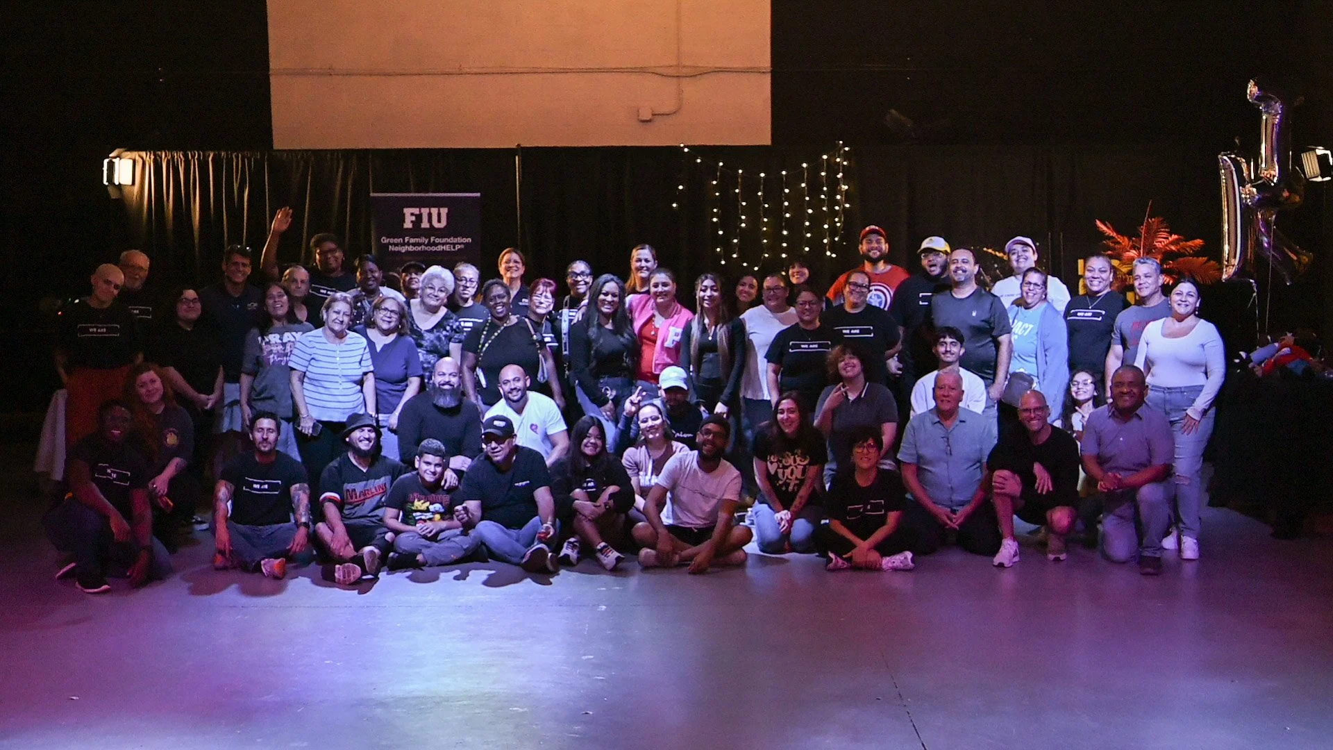 Group of people gathered on stage for a photo at an event with a banner that says 'FIU Green Family Foundation NeighborhoodHELP!'