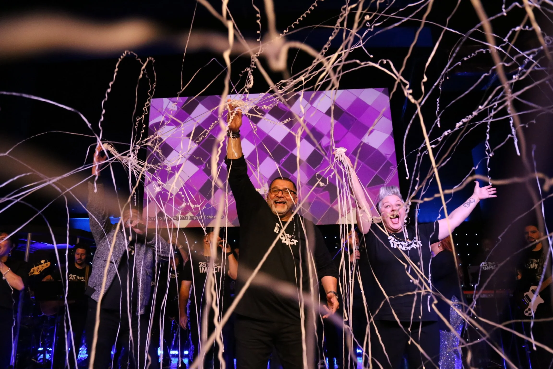 People celebrating on stage with streamers and a purple geometric background.